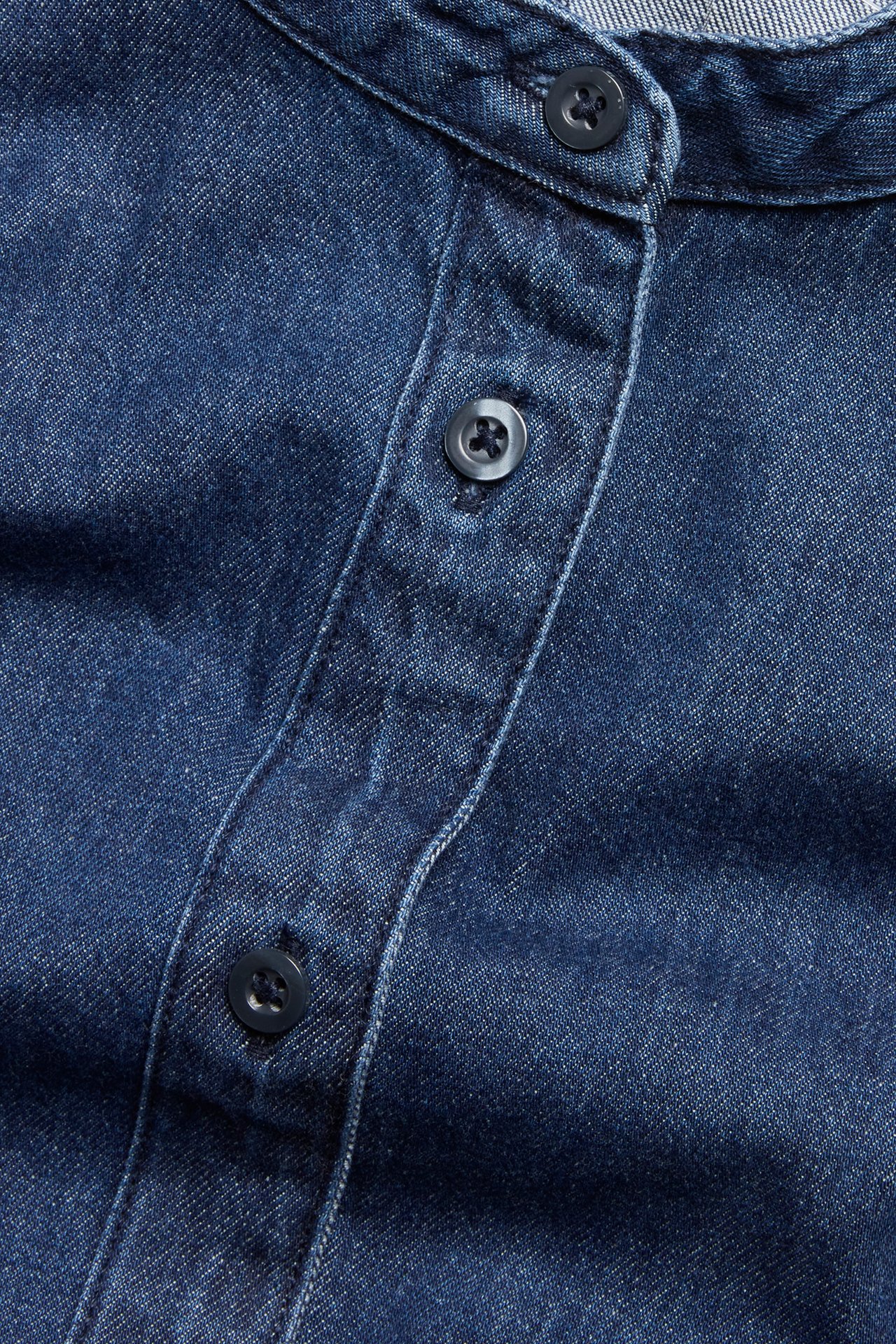 Närbild av en mörk denimblus med ståkrage och knappslå med mörka knappar.