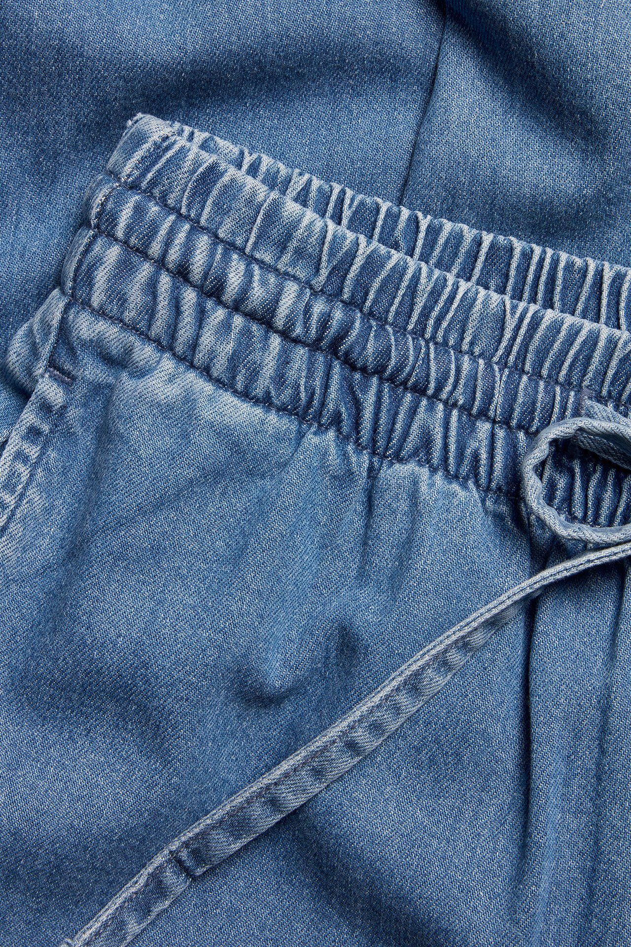 Nærbilde av lyseblå denim vide pull-on jeans med elastisk høy midje og snøring.