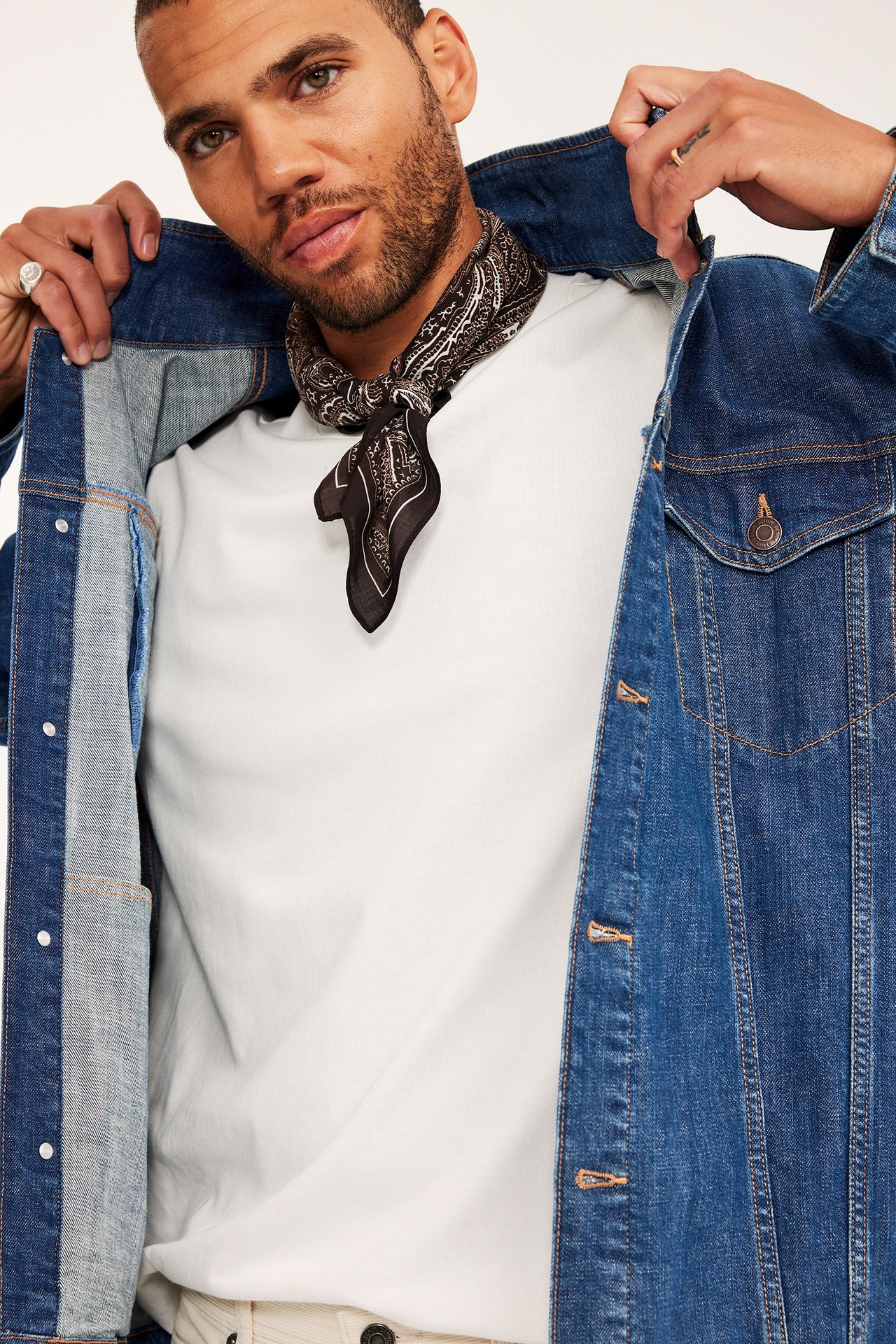 Frontvy av en man i blå jeansjacka över en vit t-shirt och svart mönstrad bandana.