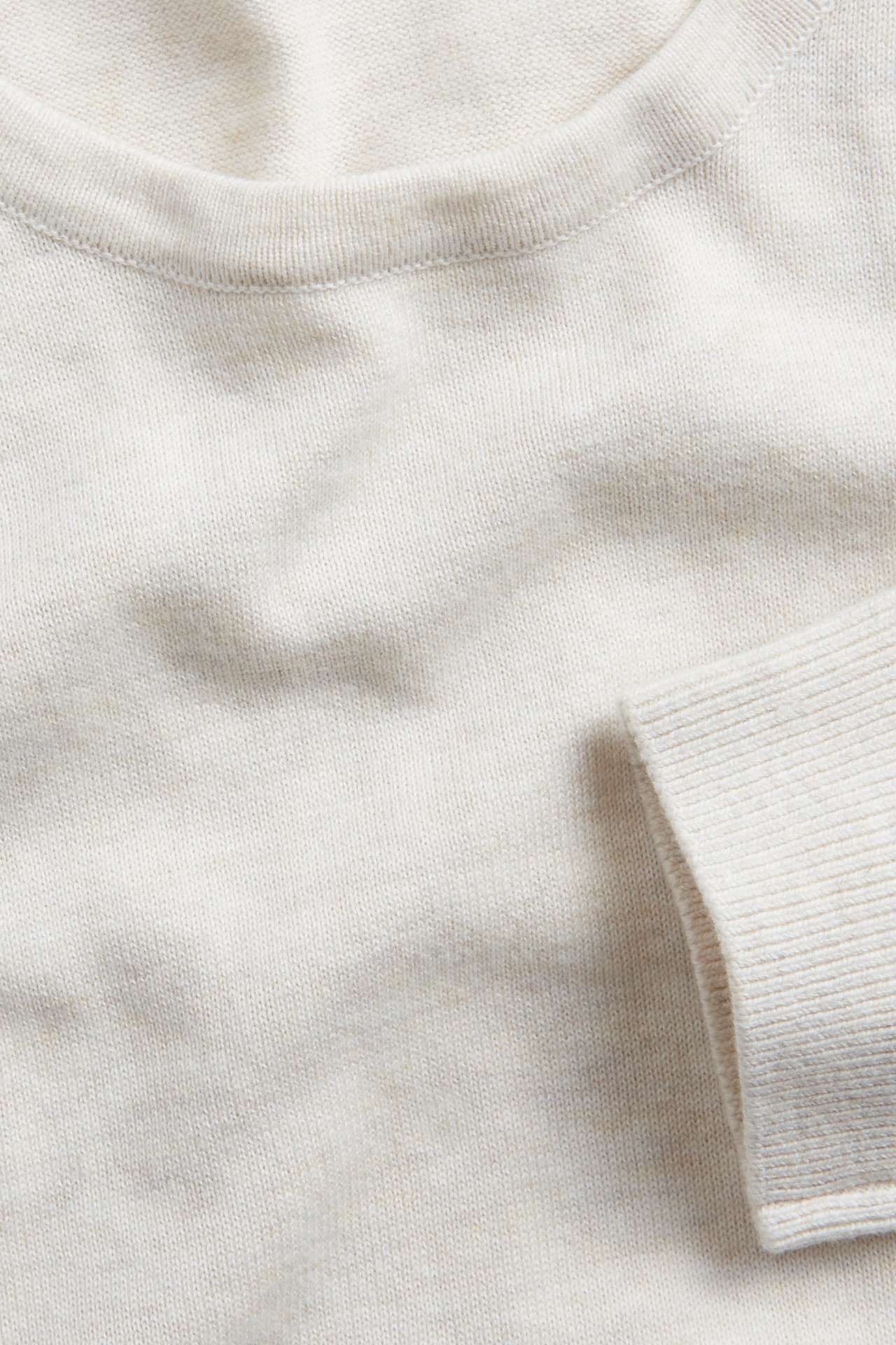 Zbliżenie na melanżowy, drobno tkany sweter bawełniany off-white z okrągłym dekoltem i ściągaczem.