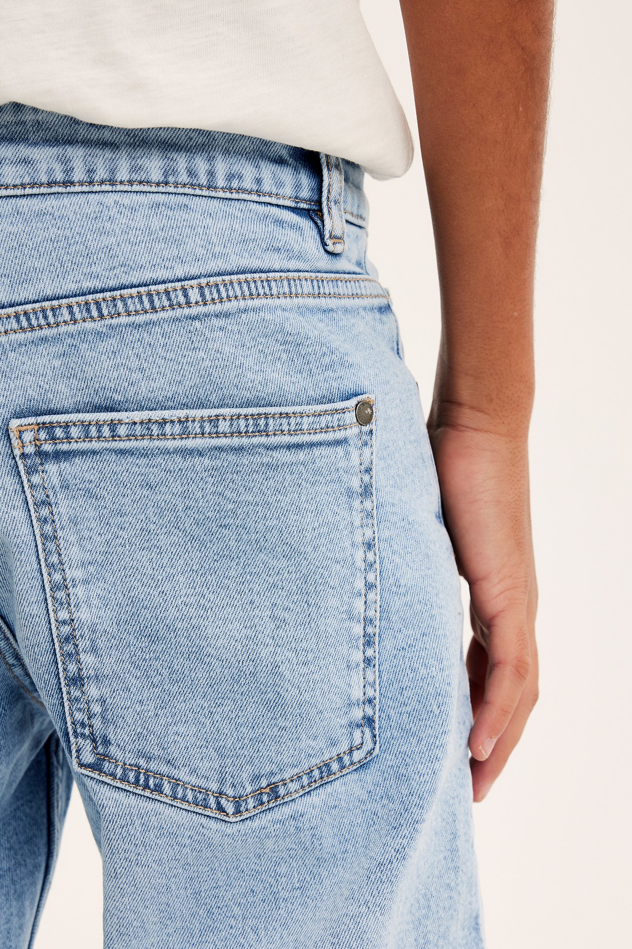 Närbild bakifrån på ett barn i ljusblå raka denimjeans med en metallnit på bakfickan.