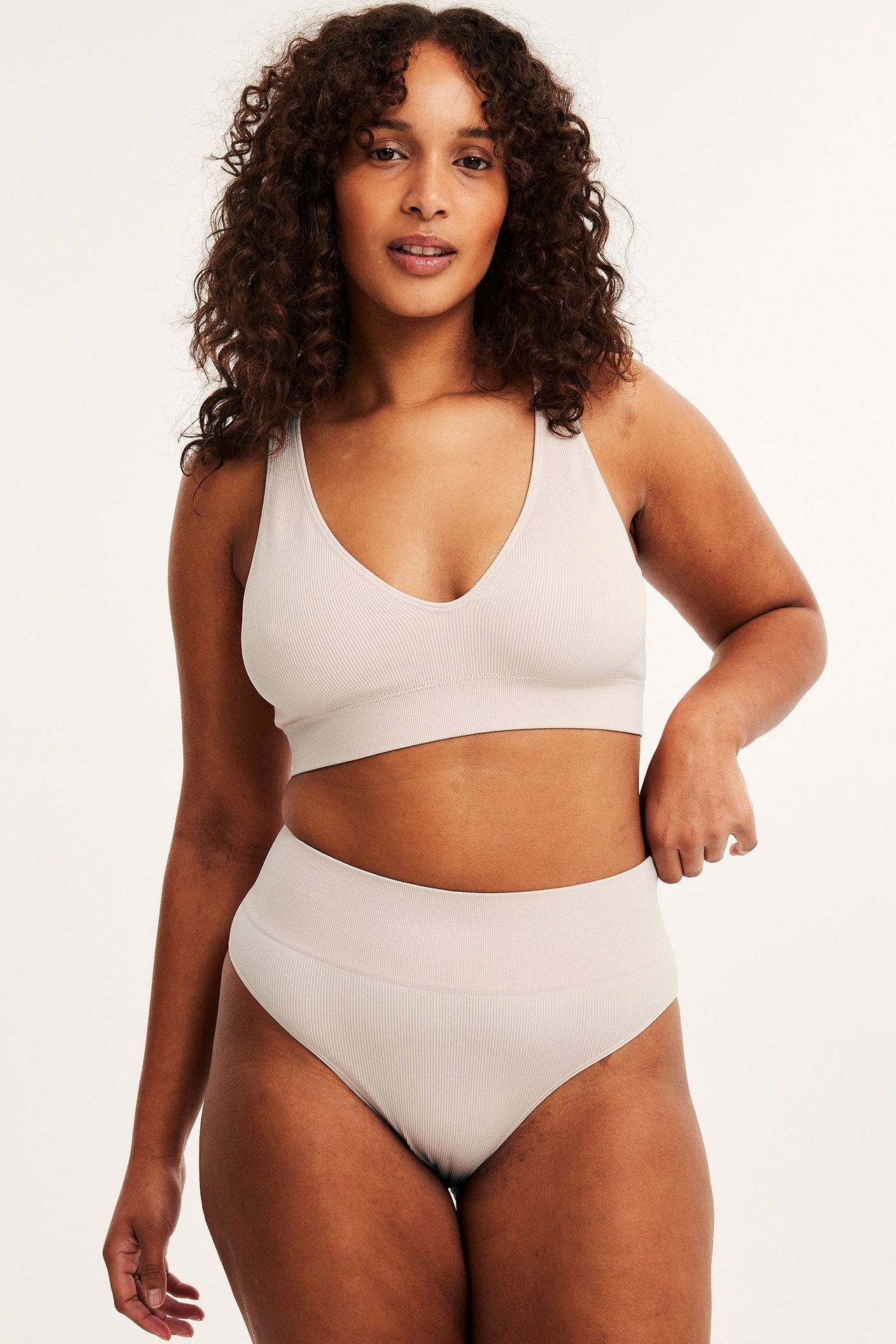 Frontbilde av en kvinne i lyserosa ribbet sømløs brazilian-truse og matchende BH.