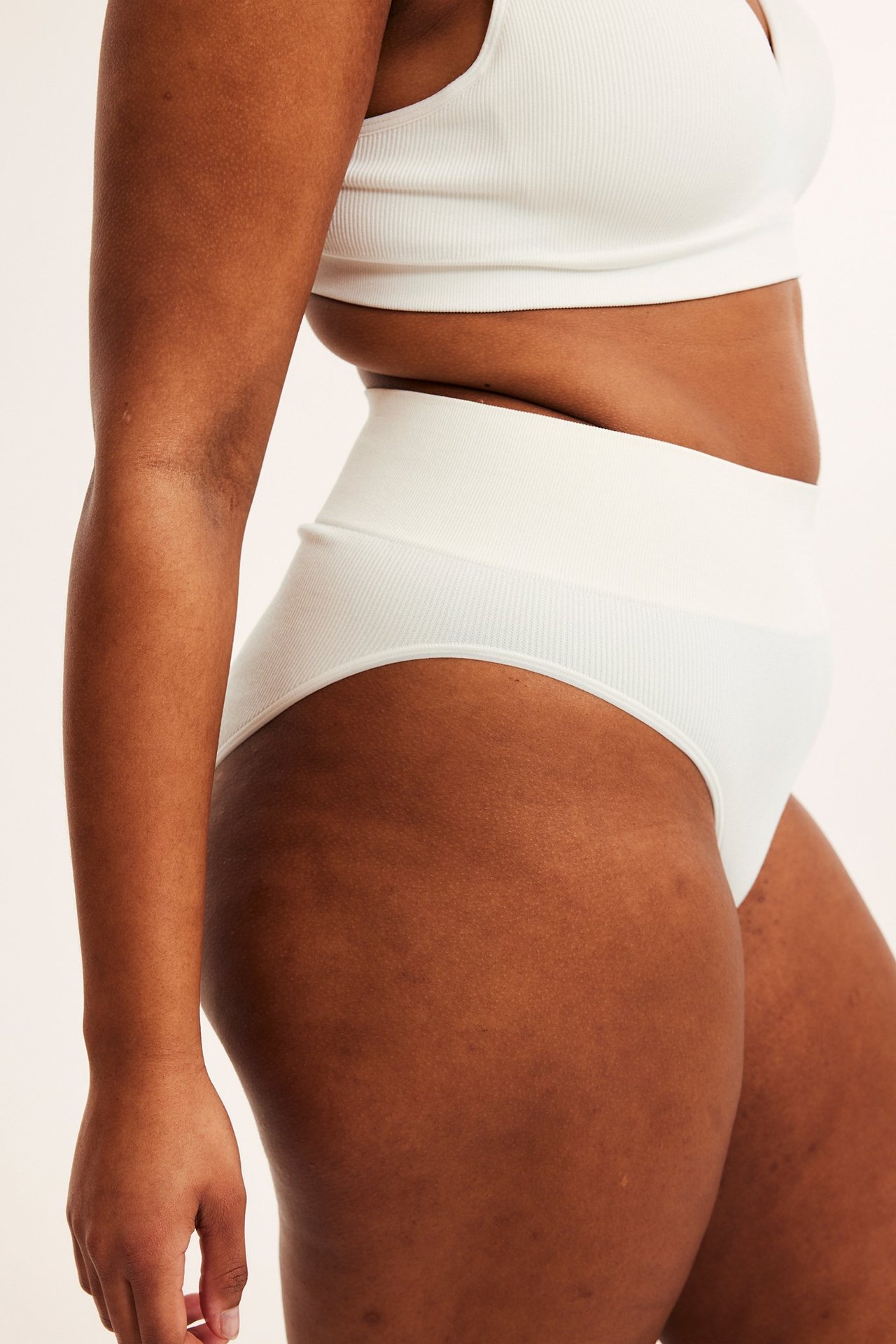 Sivukuva naisesta yllään valkoiset ribatut saumattomat brazilian-alushousut ja yhteensopiva rintaliivitoppi.