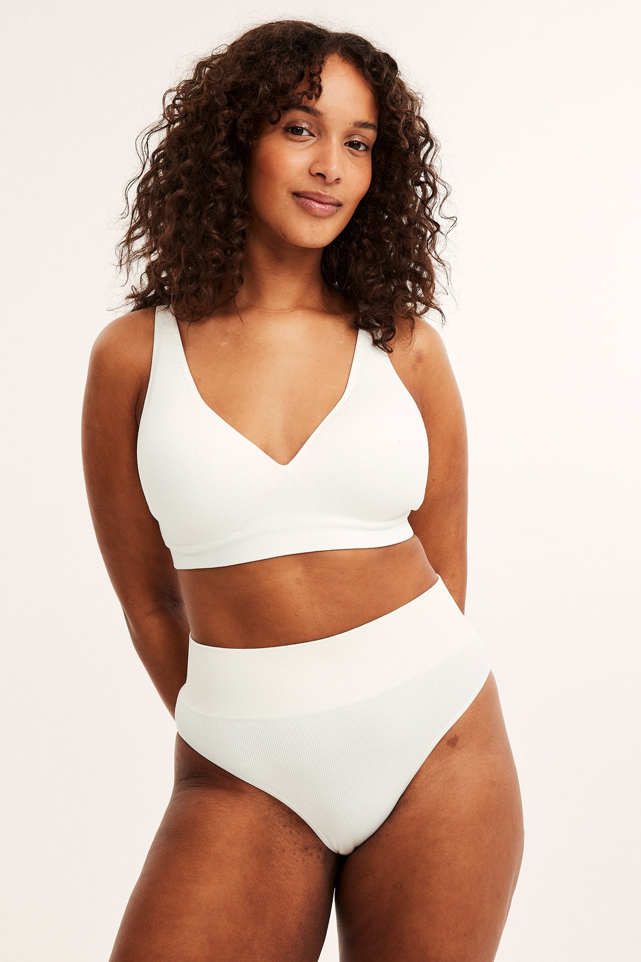 Frontbilde av en kvinne i hvit ribbet sømløs brazilian-truse og matchende ribbet BH.