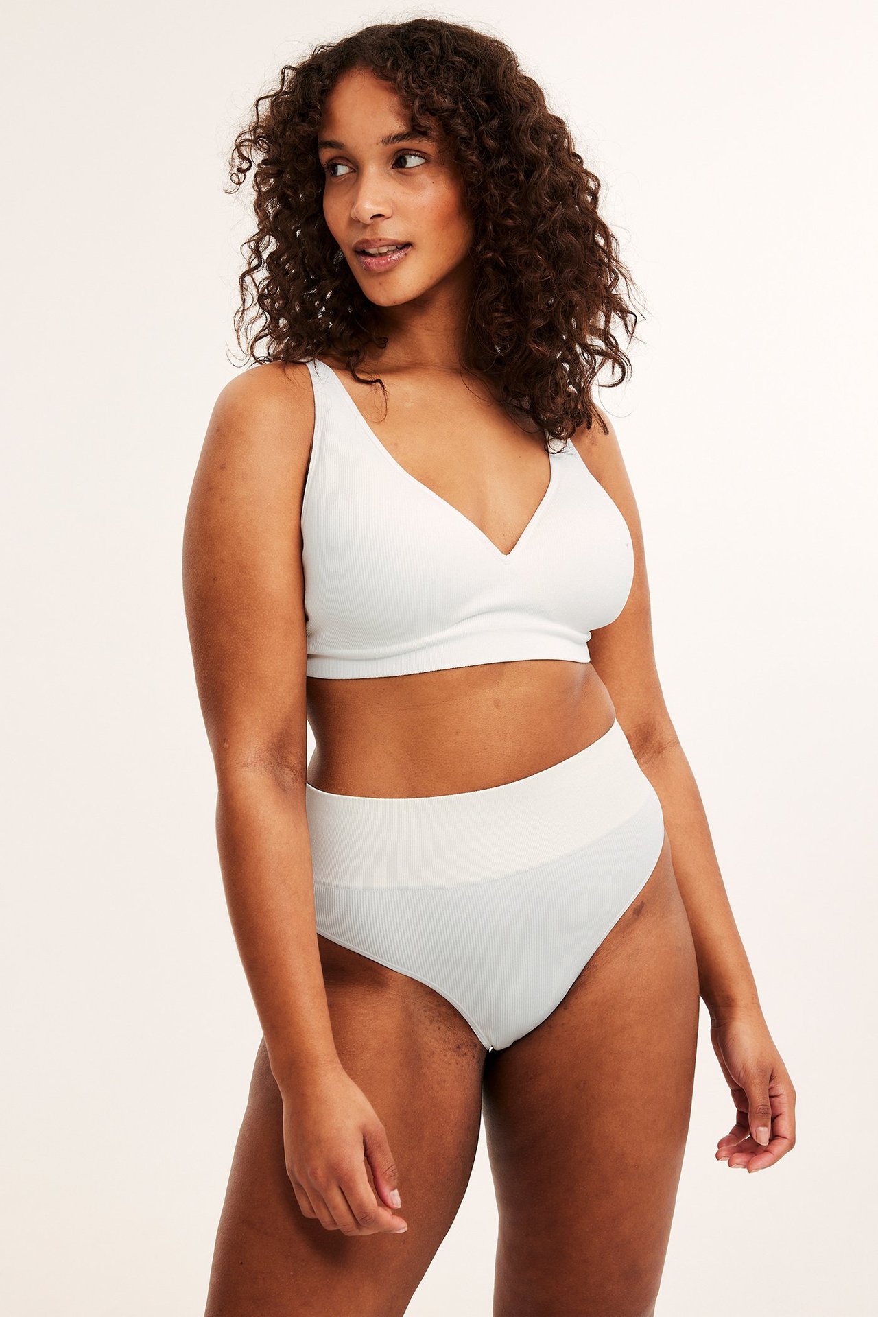 Frontvy av en kvinna i en vit ribbad sömlös V-ringad BH och matchande hög midja trosa.