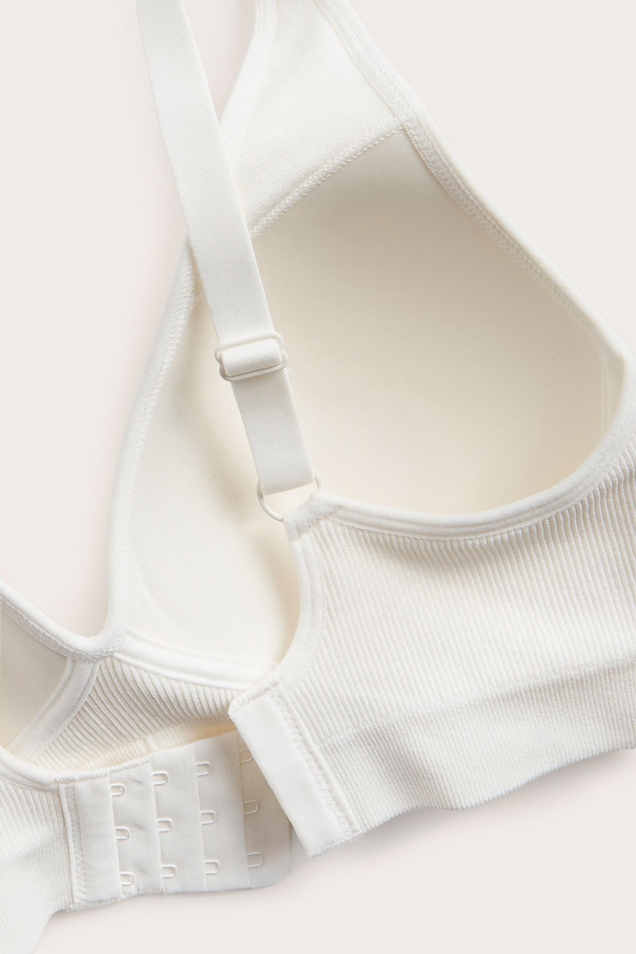 Zbliżenie białego, prążkowanego, bezszwowego biustonosza z formowanymi miseczkami i zapięciem na haftki.