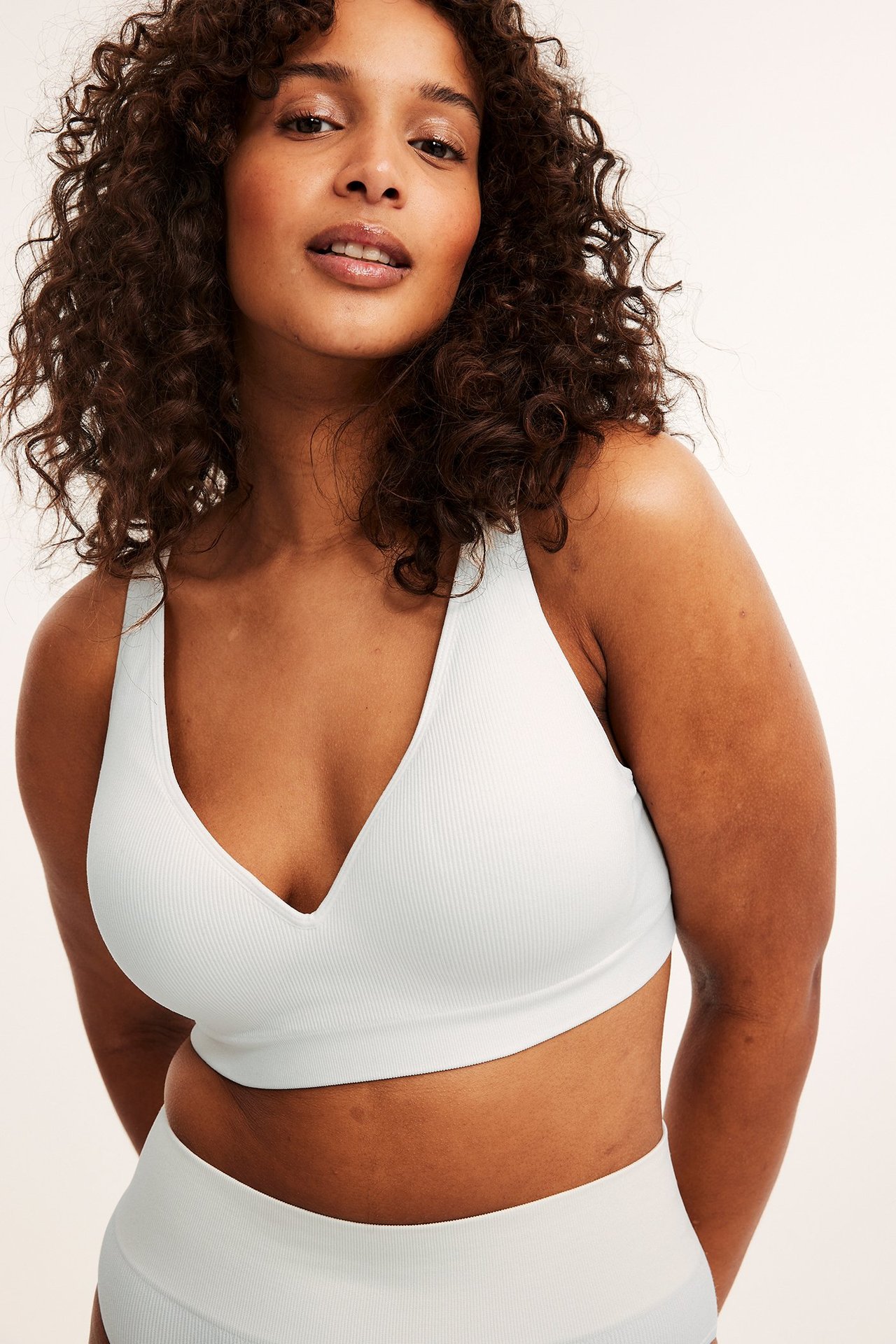 Framifrån: kvinna i vit ribbad sömlös bygellös BH med formade kupor och matchande trosa.