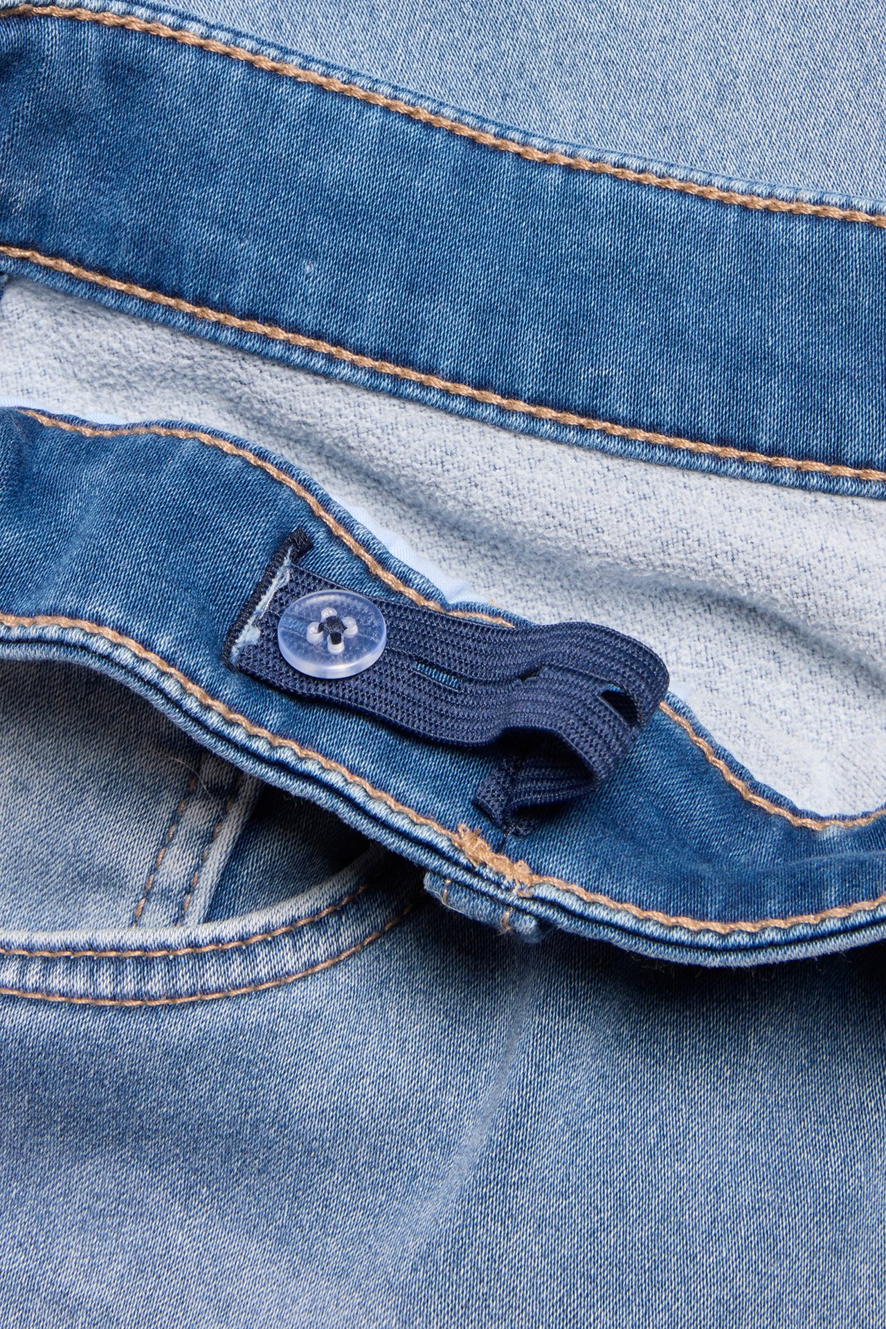 Zbliżenie na dziecięce jasnoniebieskie jeansy jogger denim z regulowaną gumką w pasie i guzikiem.