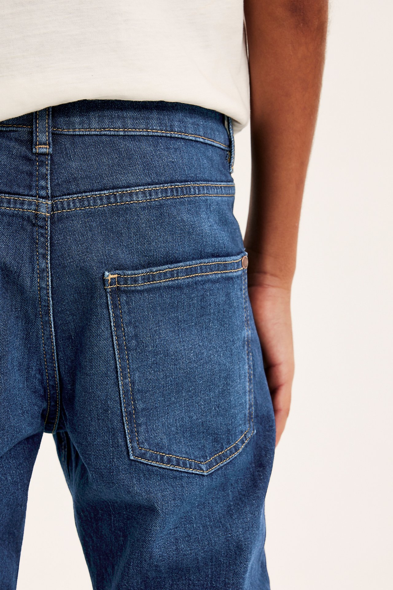 Lähikuva takaa lapsen tummansinisistä slim fit mid-waist farkuista takataskulla, valkoisen t-paidan päällä.