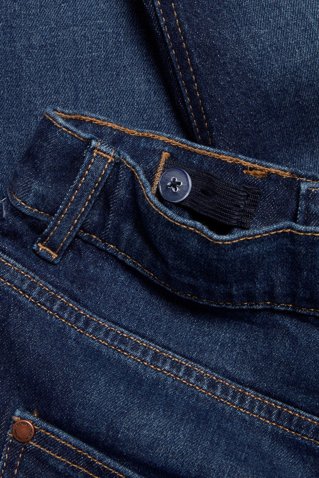 Zbliżenie na ciemnoniebieskie dżinsy slim z pomarańczowymi szwami i regulowaną elastyczną talią z guzikiem.