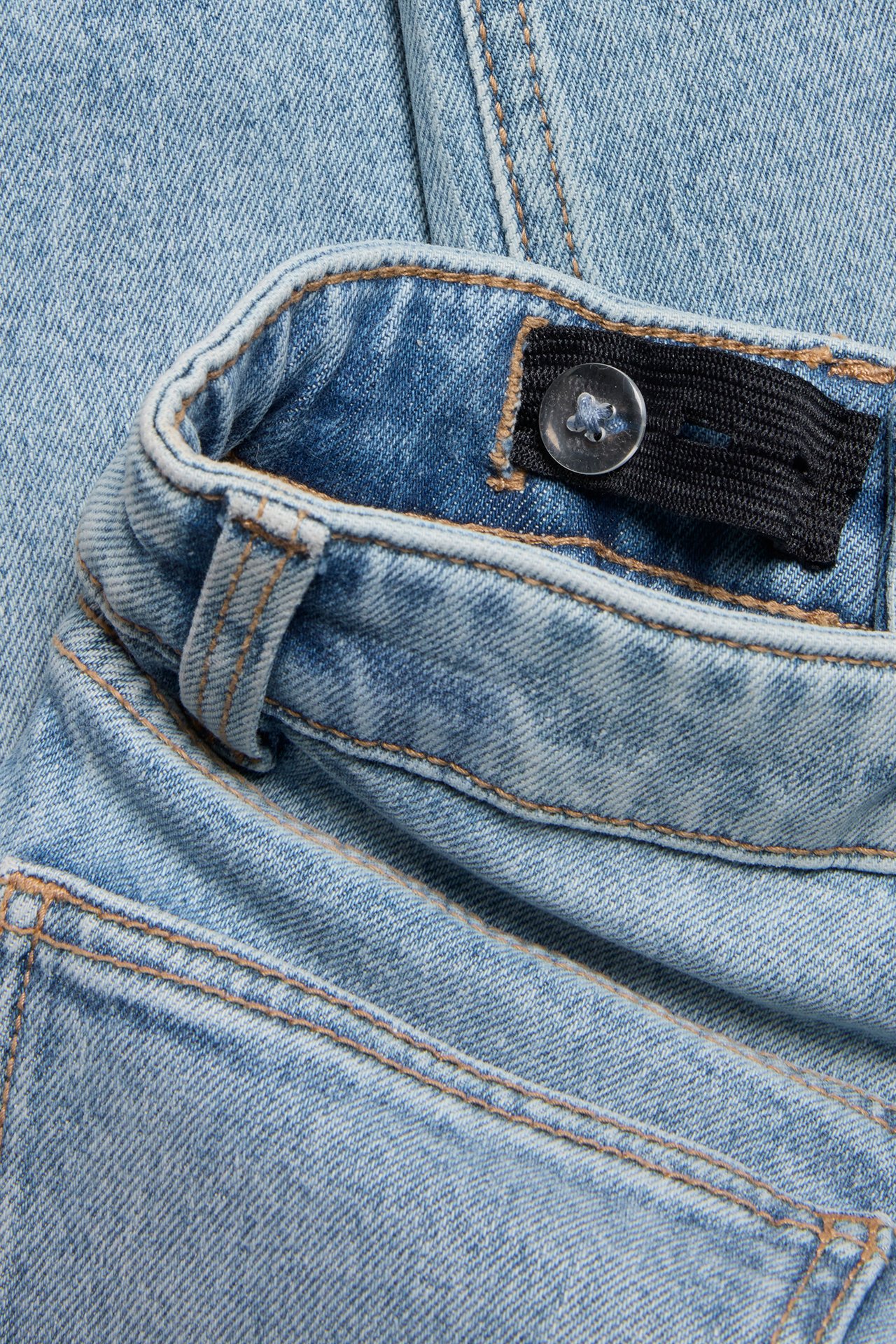 Närbild av ljusblå slim jeans i denim med justerbar resår i midjan och knapp.