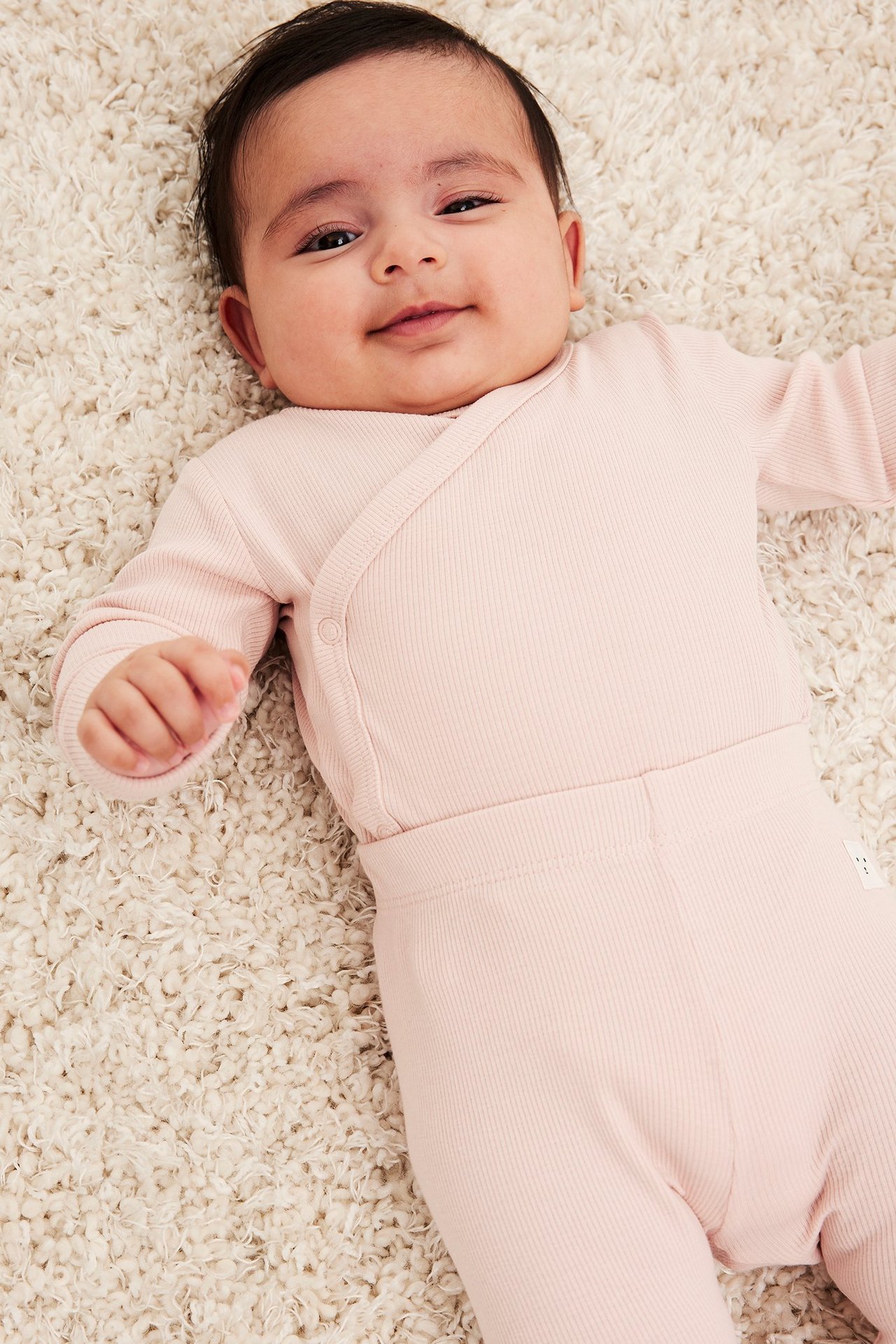 Ylhäältä kuvattu vauva yllään vaaleanpunainen ribattu kietaisubody neppareilla ja yhteensopivat housut.