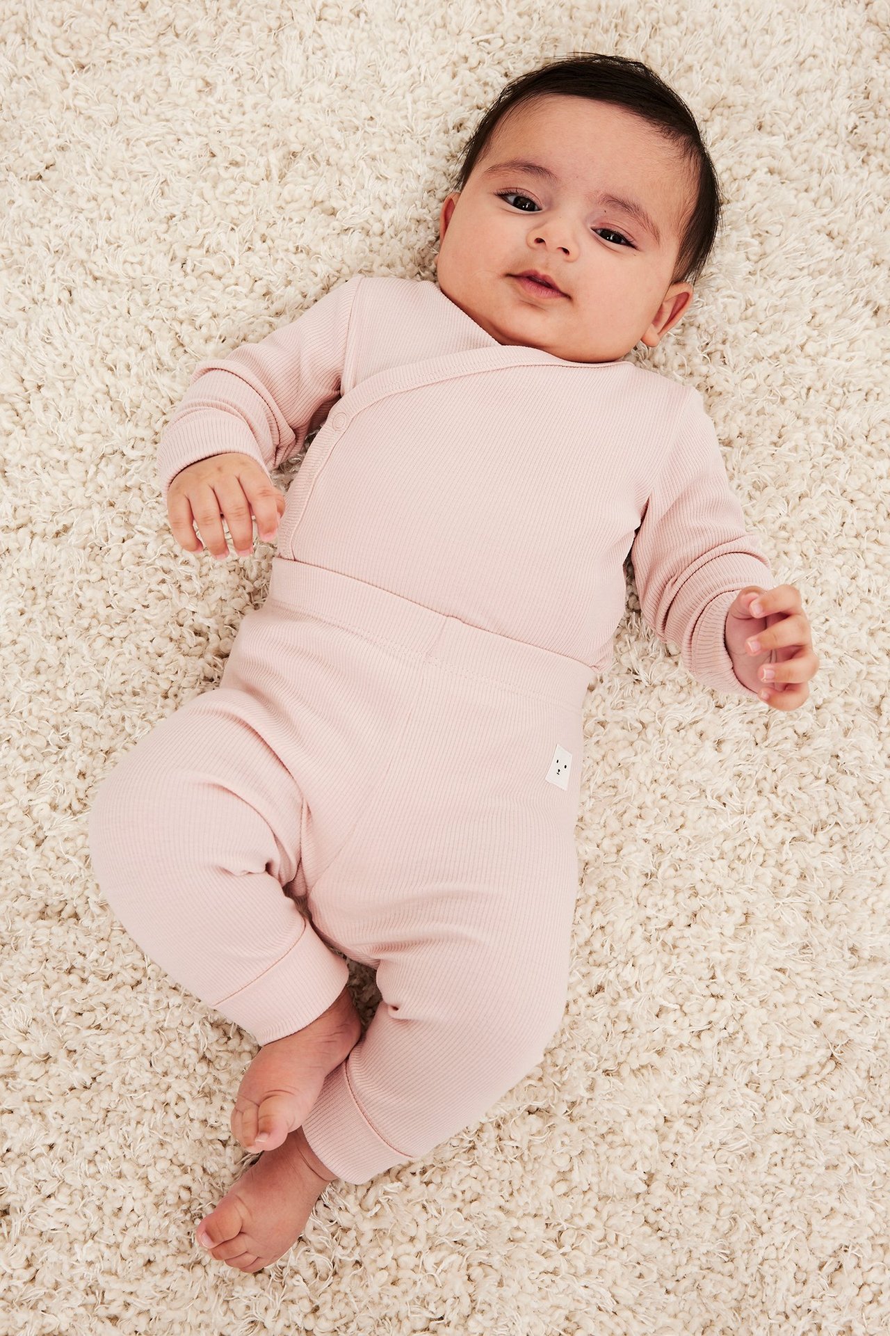 Uppifrån-vy av en baby i ljusrosa ribbade leggings och matchande omlott-topp.