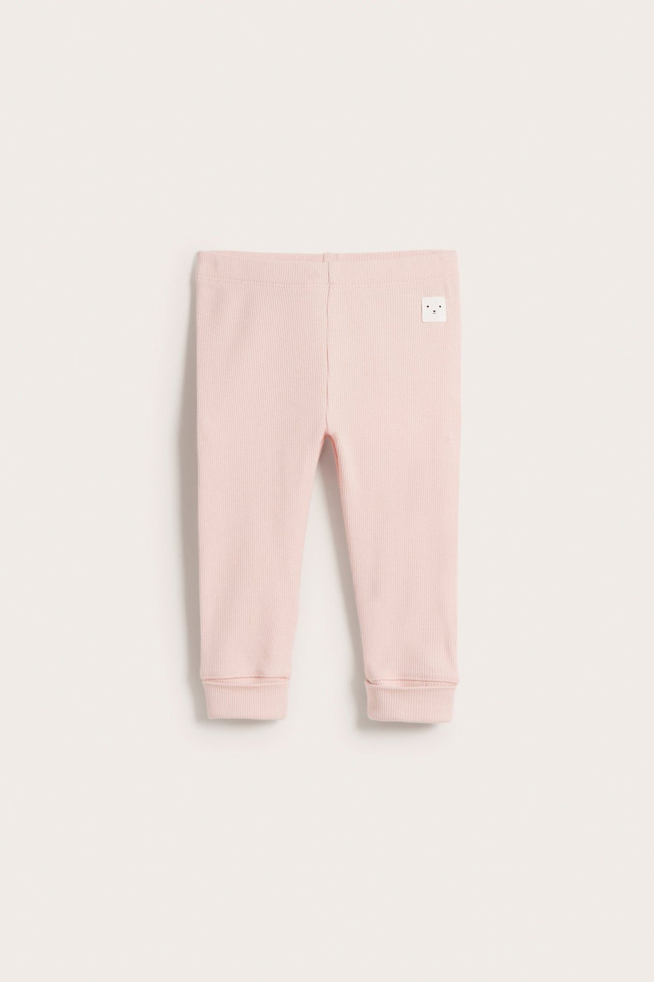 Frontvy av ljusrosa ribbade baby leggings med resår i midjan och breda muddar.
