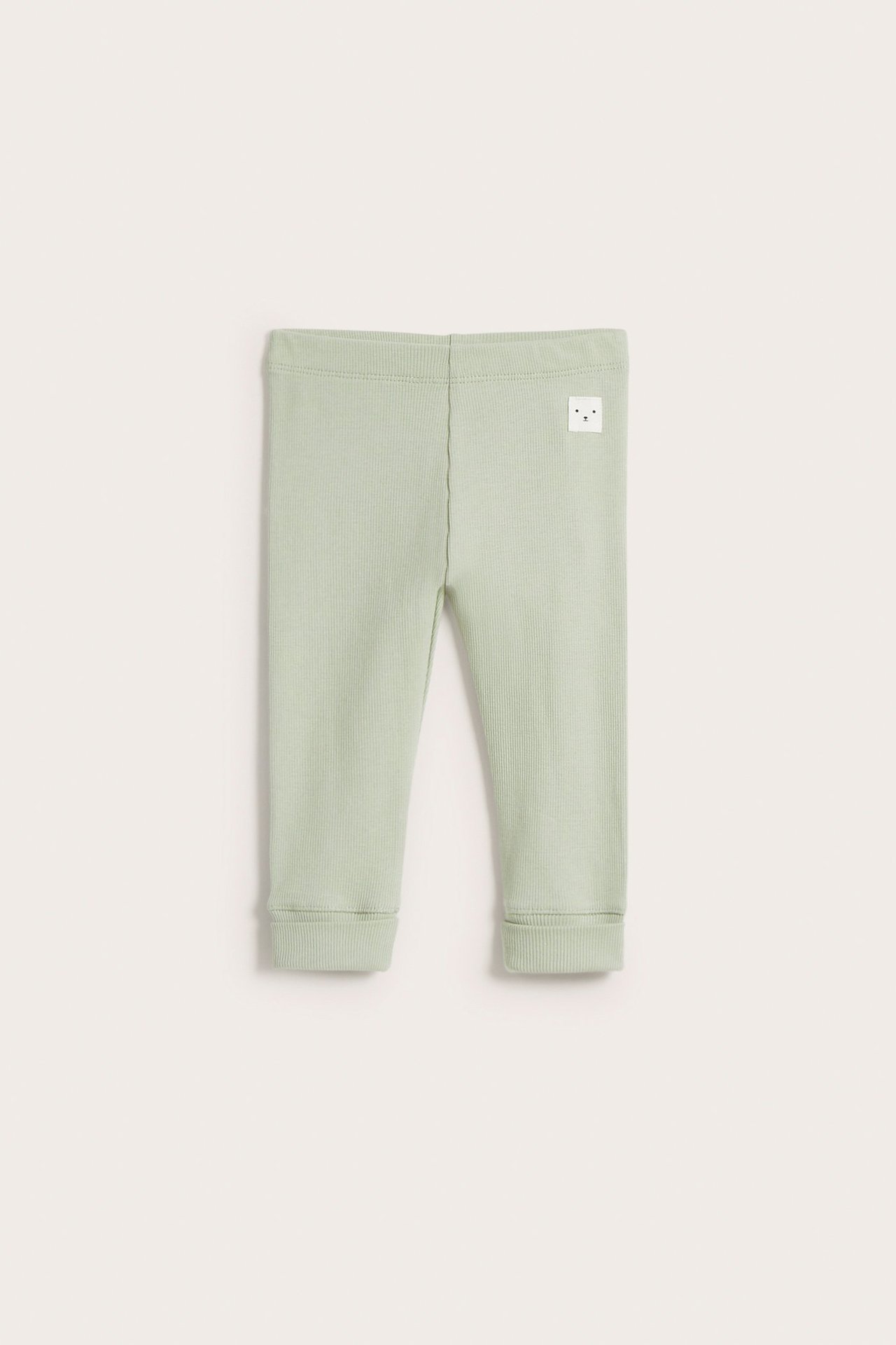 Frontvy av ljusgröna ribbade baby leggings med generösa muddar och en liten vit ansiktslapp.