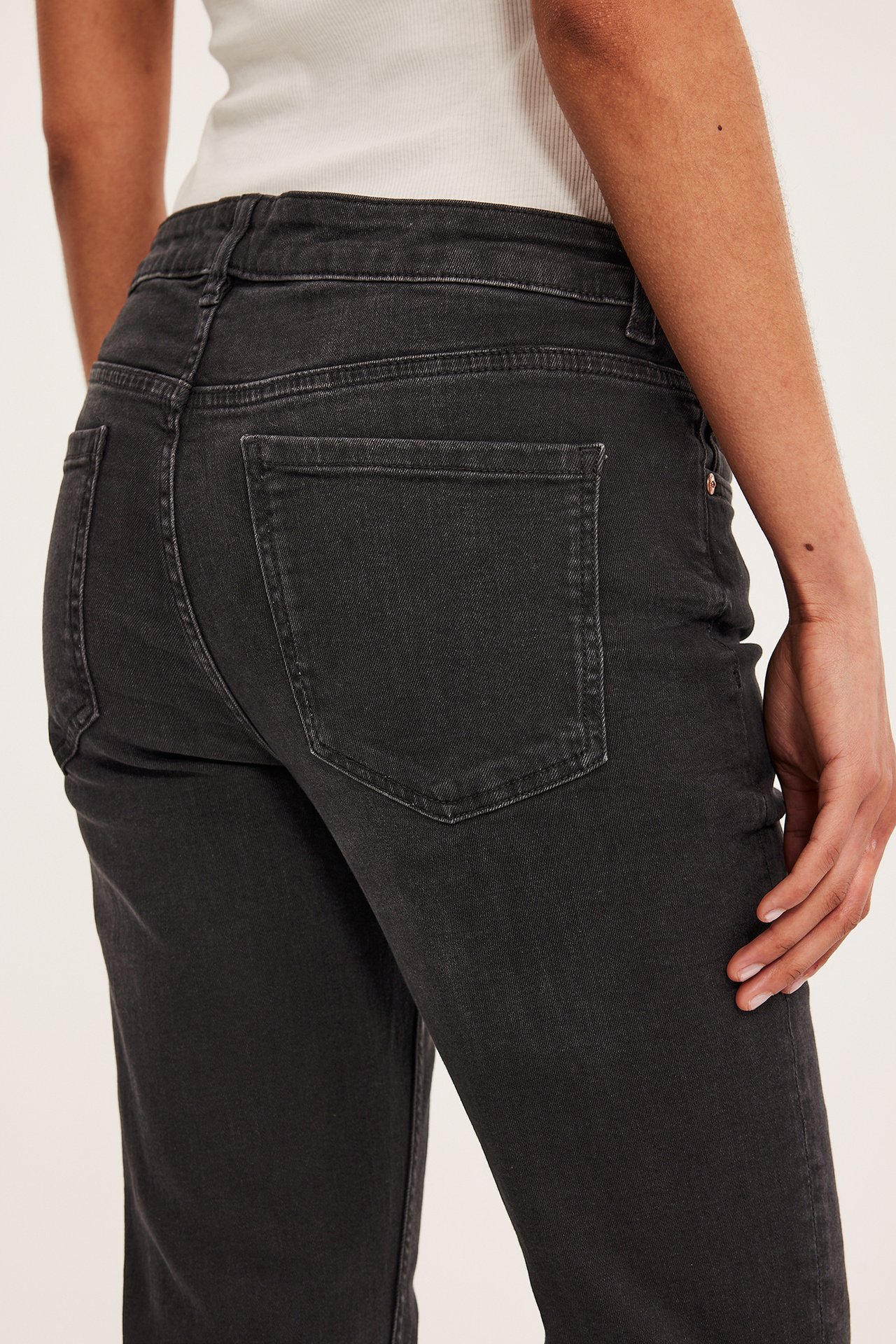 Lähikuva naisen selästä mustissa matalavyötäröisissä bootcut-farkuissa ja valkoisessa ribbipaidassa.