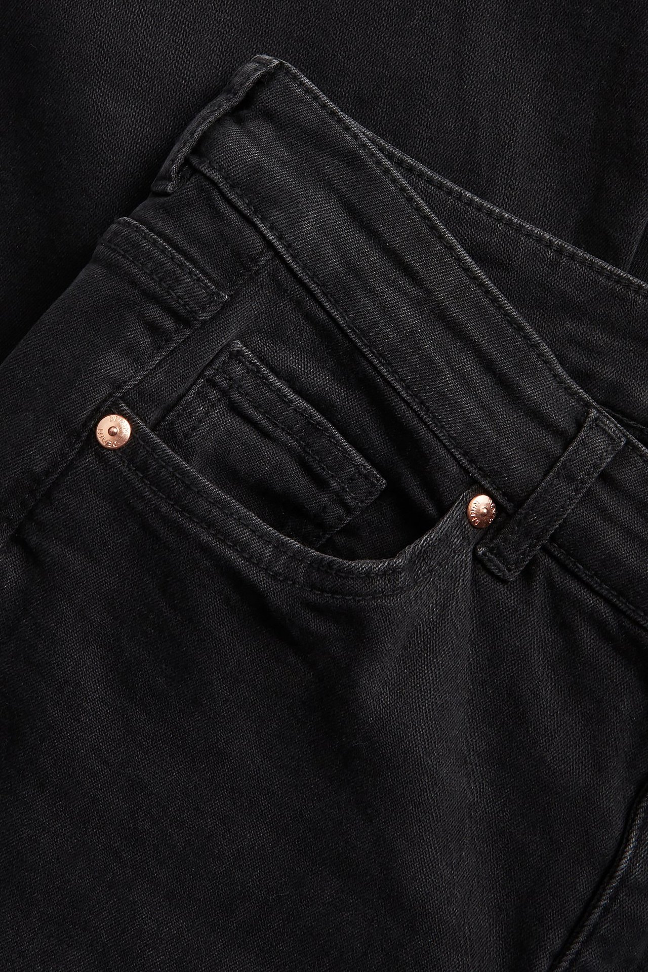 Zbliżenie na czarne jeansy bootcut z niskim stanem, przednią kieszenią i miedzianymi nitami.