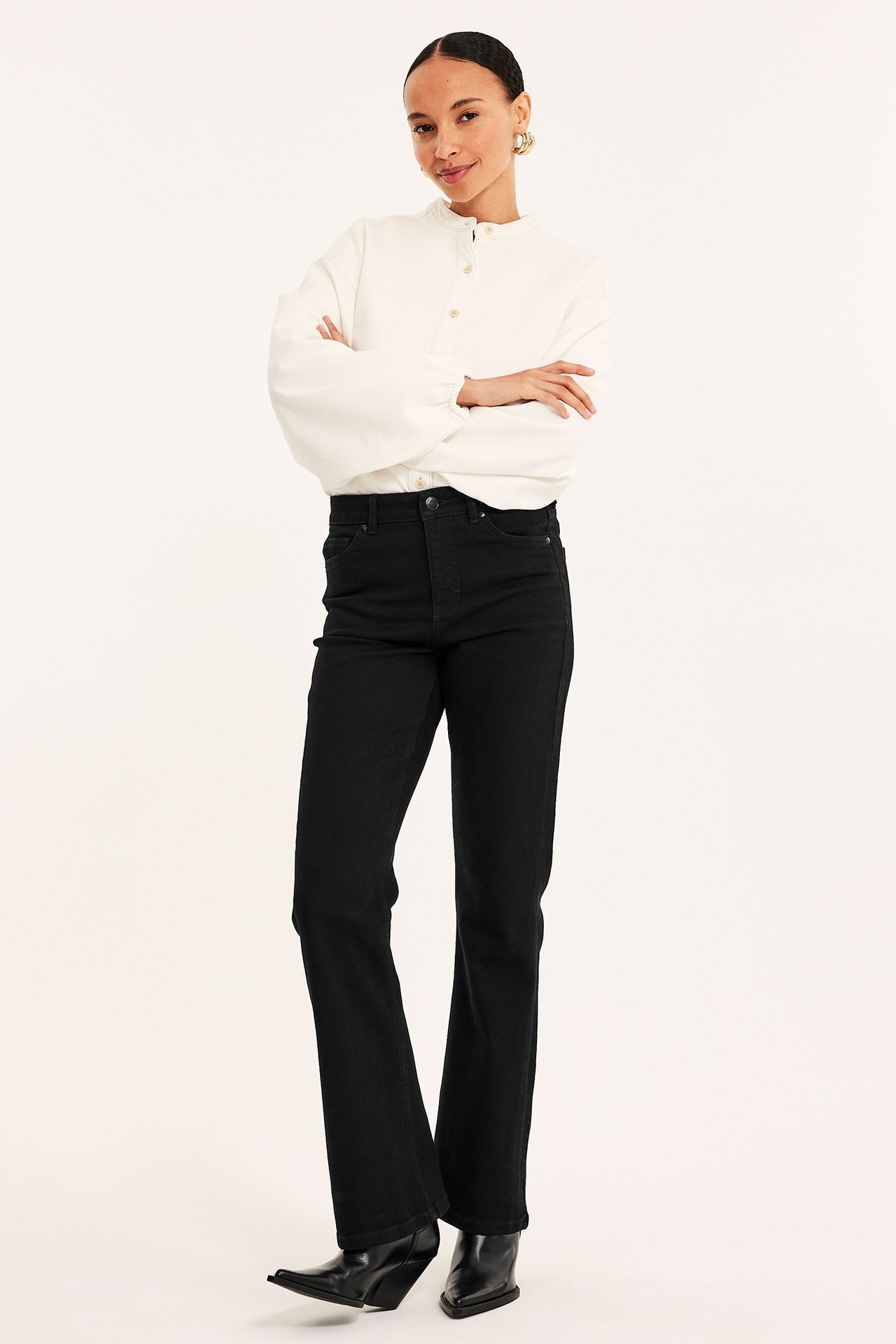 Framifrån: Kvinna i svarta flare jeans med normal midja, vit långärmad blus och svarta spetsiga stövlar.