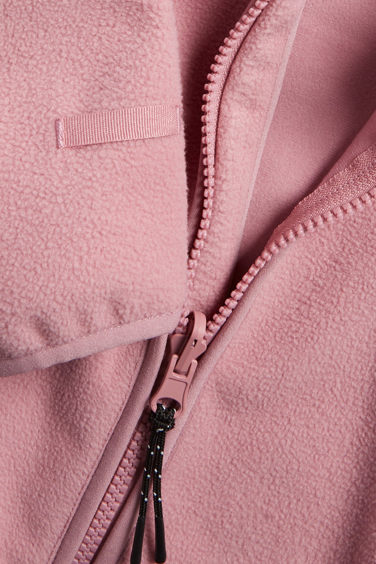 Nærbilde av en rosa ensfarget fleecejakke med rosa glidelås og svart-hvit snor.