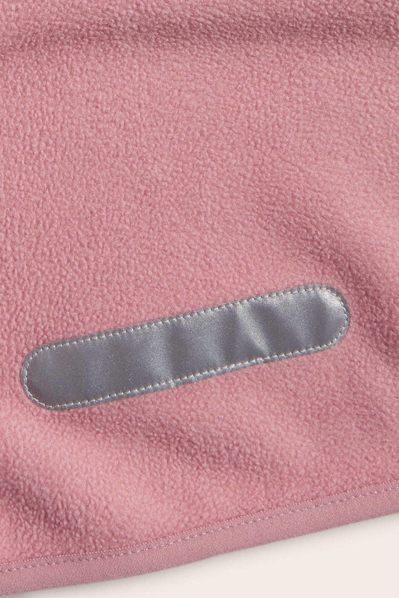 Nærbilde av rosa fleecejakke-stoff med en grå refleksstripe.