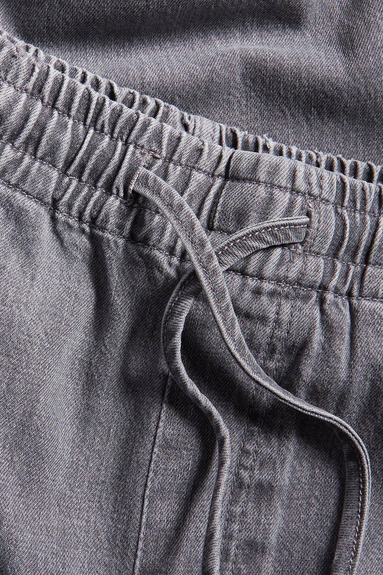Lähikuva harmaista denim-leveistä farkuista, joissa joustava korkea vyötärö ja kiristysnyöri.