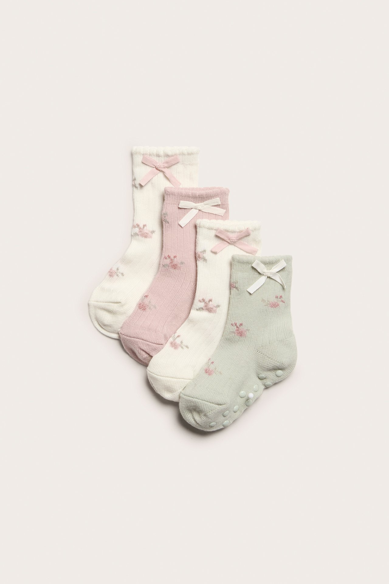 Uppifrån: Fyra par babystrumpor i offwhite, rosa, grönt, med blommönster, rosetter och antislip-sulor.