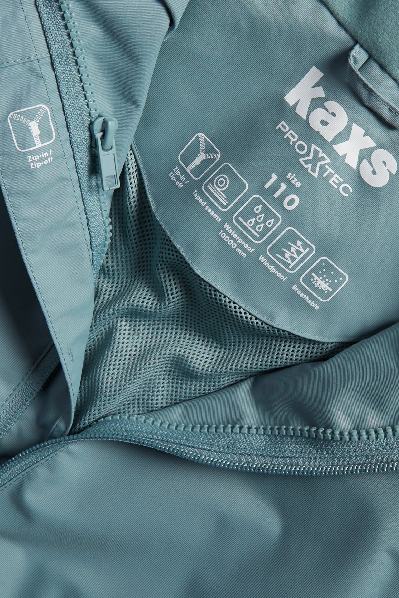 Zbliżenie niebieskiej wodoodpornej kurtki dziecięcej, ukazujące zamek błyskawiczny, podszewkę z siatki i etykietę Kaxs Proxtec.