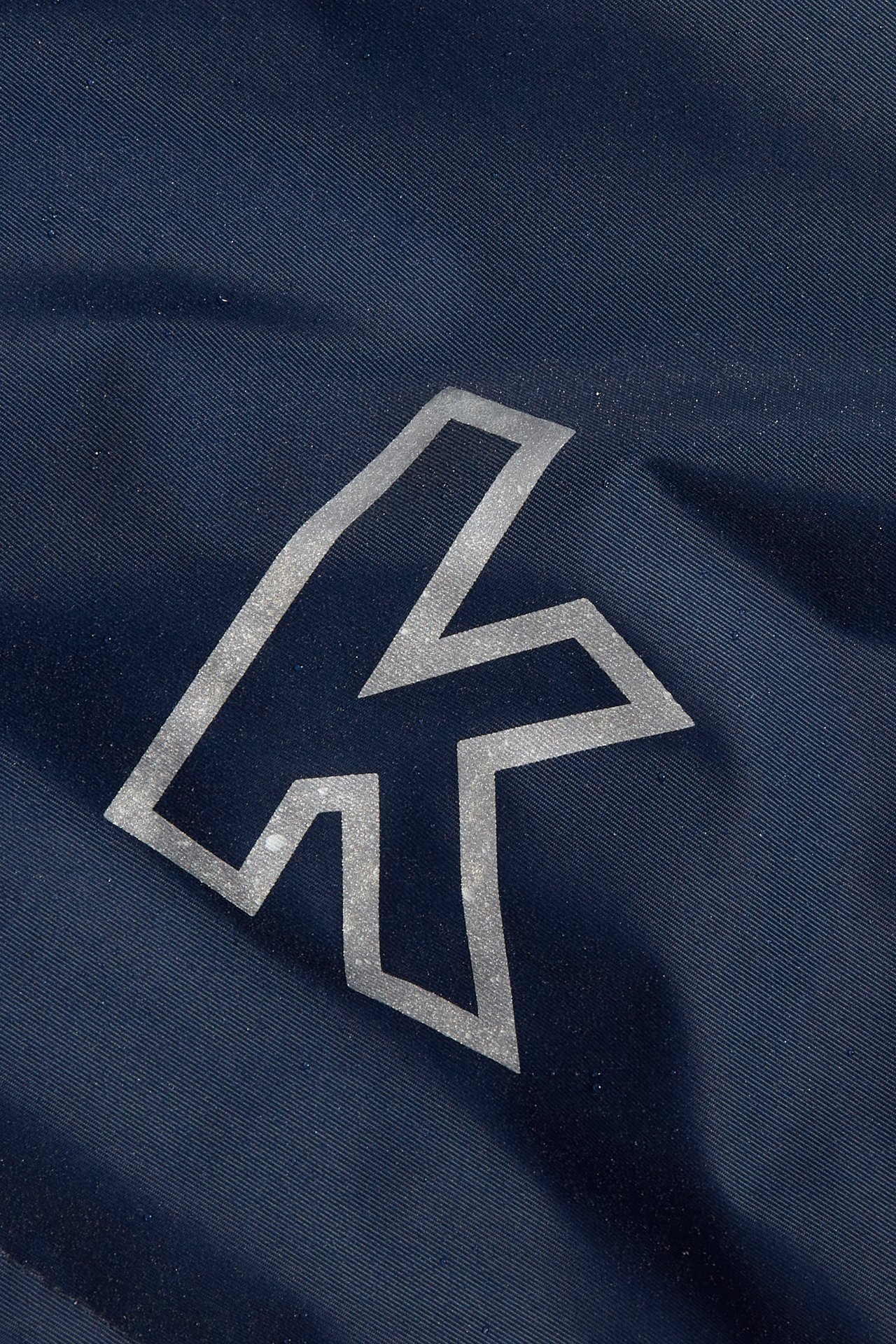 Zbliżenie na ciemnoniebieską wodoodporną kurtkę softshell z srebrno-szarym odblaskowym logo Kaxs.