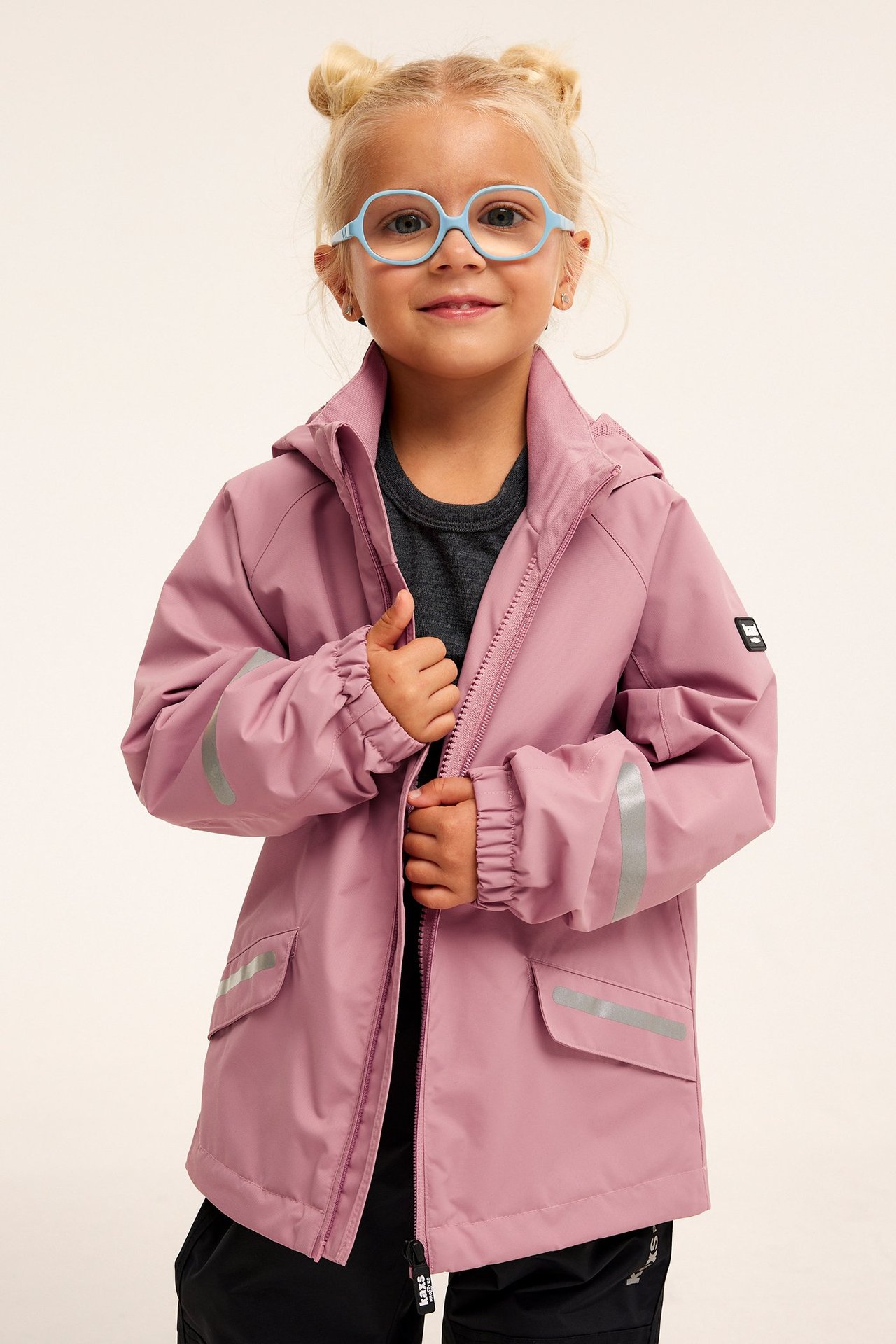 Dziecko w różowej wodoodpornej kurtce z odblaskami, szarym t-shircie i niebieskich okularach.