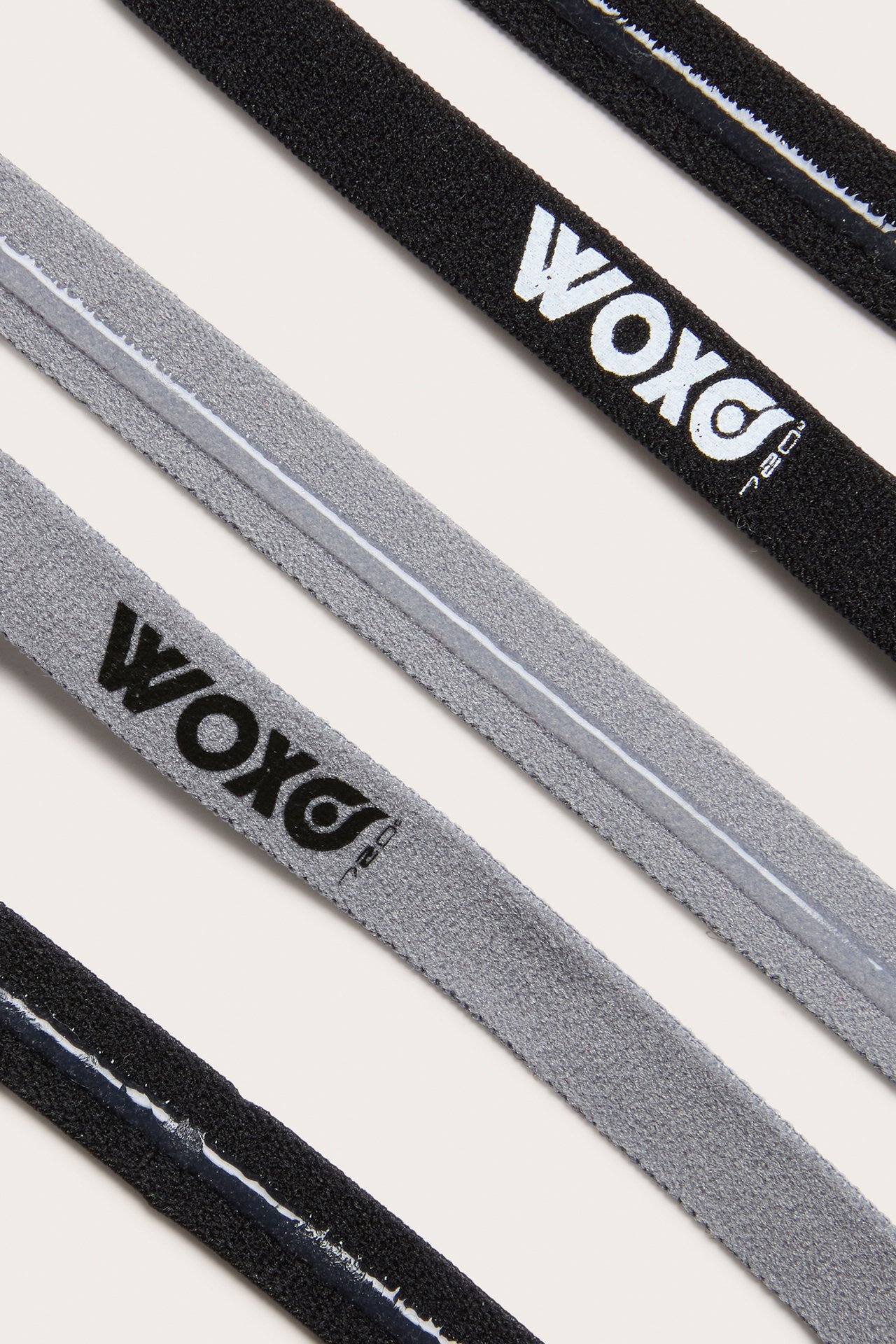 Nærbilde av tre polyesterhårbånd: svart med hvit Woxo-logo, grått med svart Woxo-logo og svart.