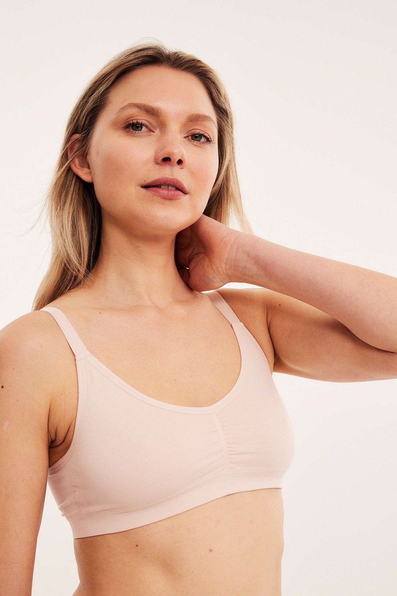 Frontvy av en kvinna i en ljusrosa sömlös mjuk BH med V-ringning och rynkad detalj.