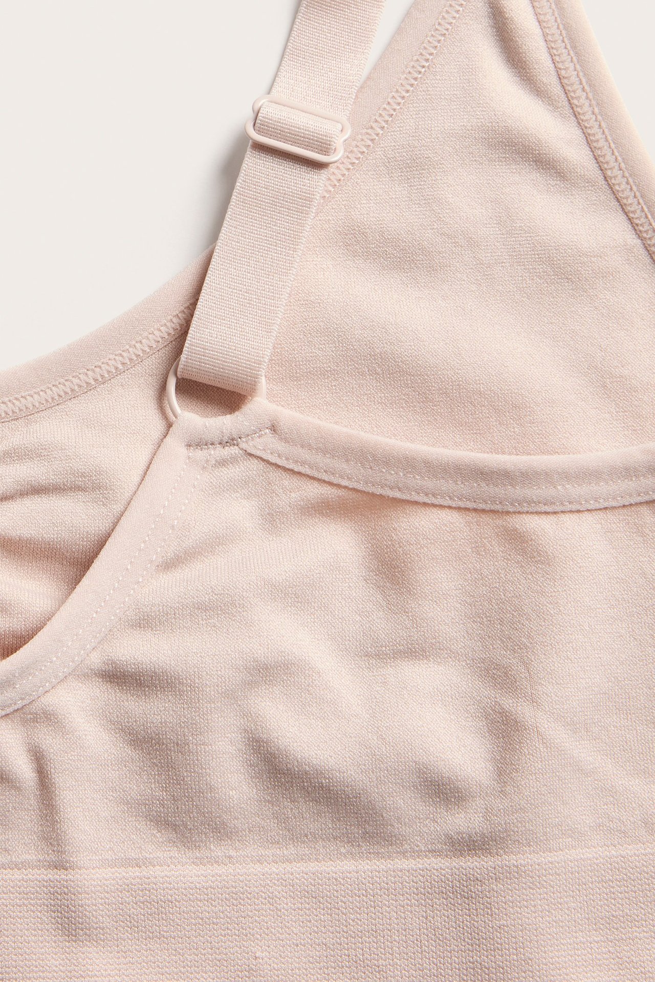 Zbliżenie na jasnoróżowy, bezszwowy biustonosz z regulowanym ramiączkiem.