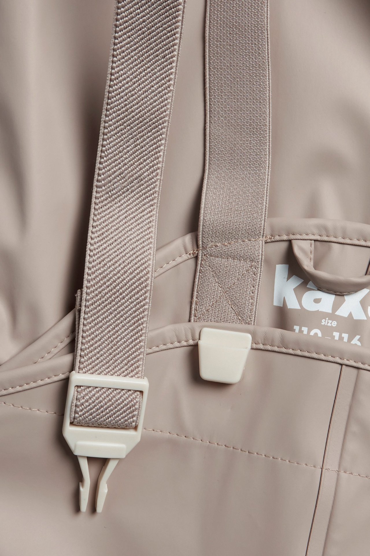 Zbliżenie na beżowe spodnie przeciwdeszczowe dla dzieci z regulowanymi elastycznymi szelkami i plastikowymi klamrami.