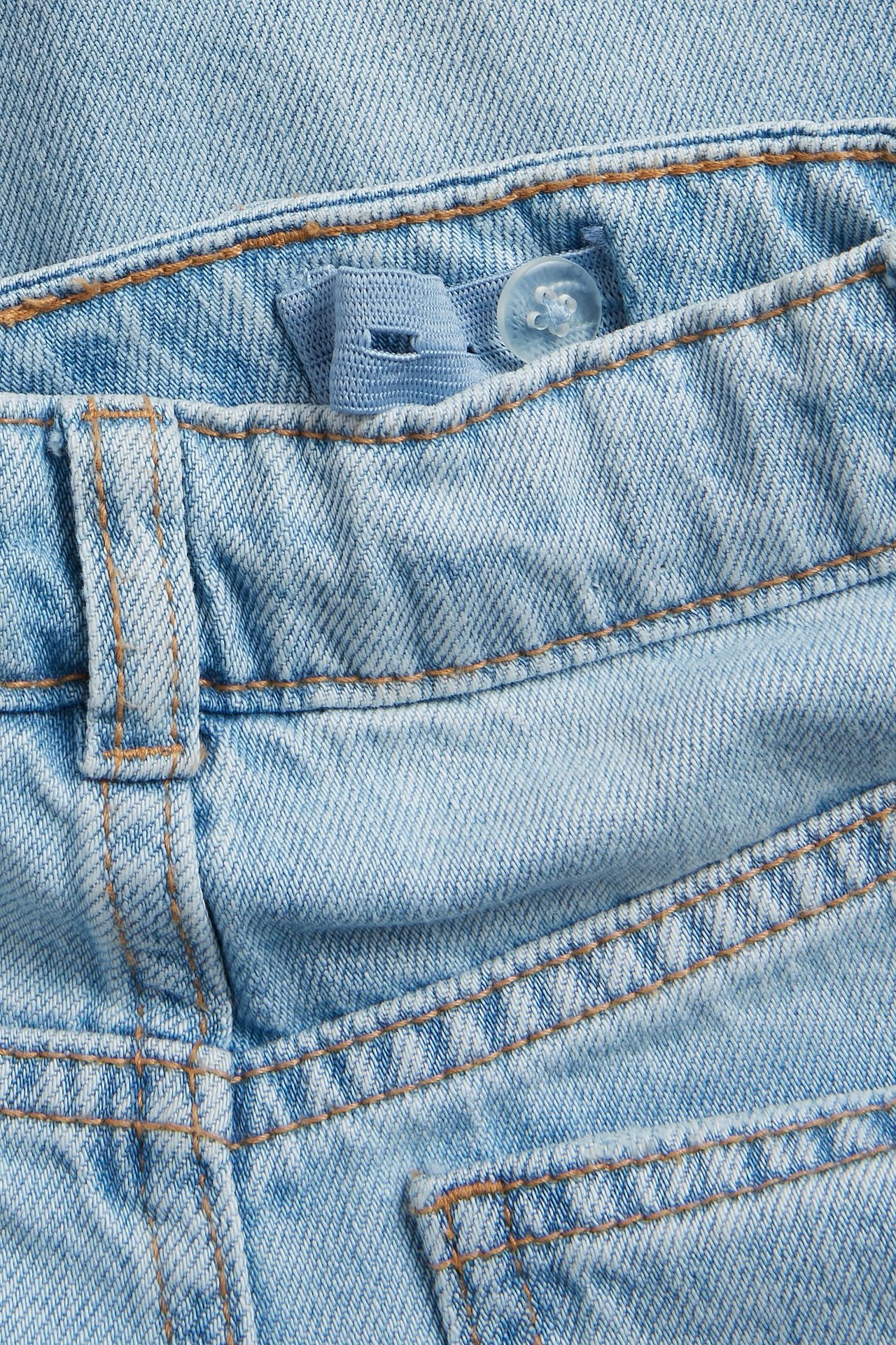Zbliżenie na jasnoniebieskie dżinsy dziecięce z szerokimi nogawkami, pokazujące regulowaną gumkę w pasie z guzikiem.