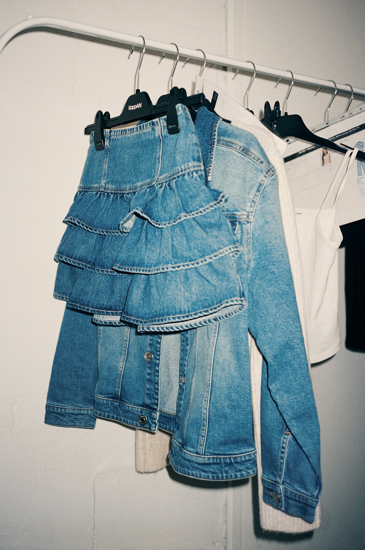 Frontvy: ljus denim volangkjol, denimjacka, beige kofta och vitt linne på galgar.