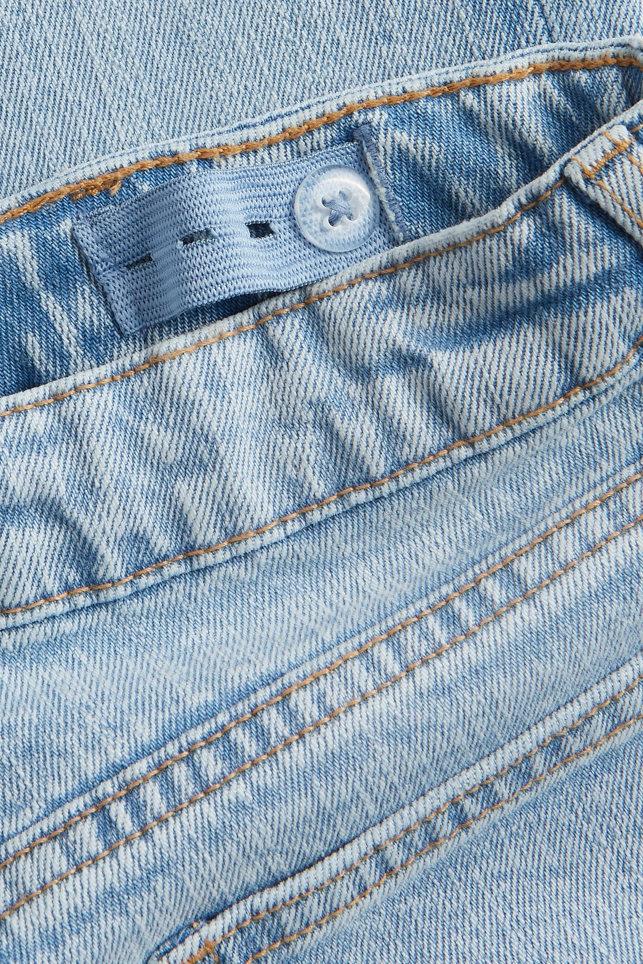 Lähikuva vaaleansinisistä bootcut-farkkujen vyötäröstä säädettävällä kuminauhalla ja napilla.