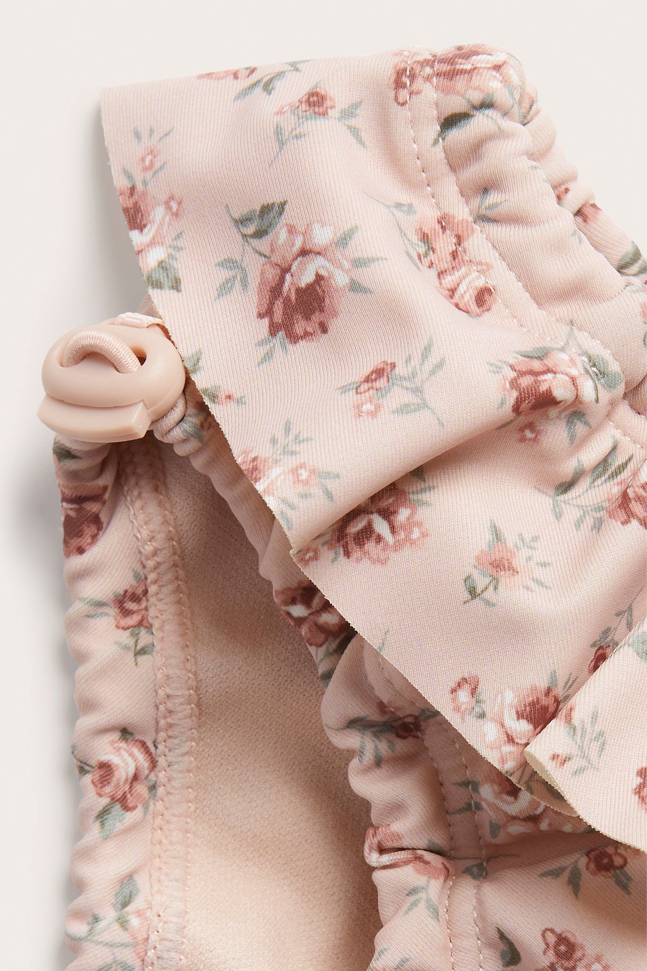 Lähikuva vaaleanpunaisista kukkakuvioisista uimahousuista, joissa on röyhelövyötärö ja nyörinpysäytin.