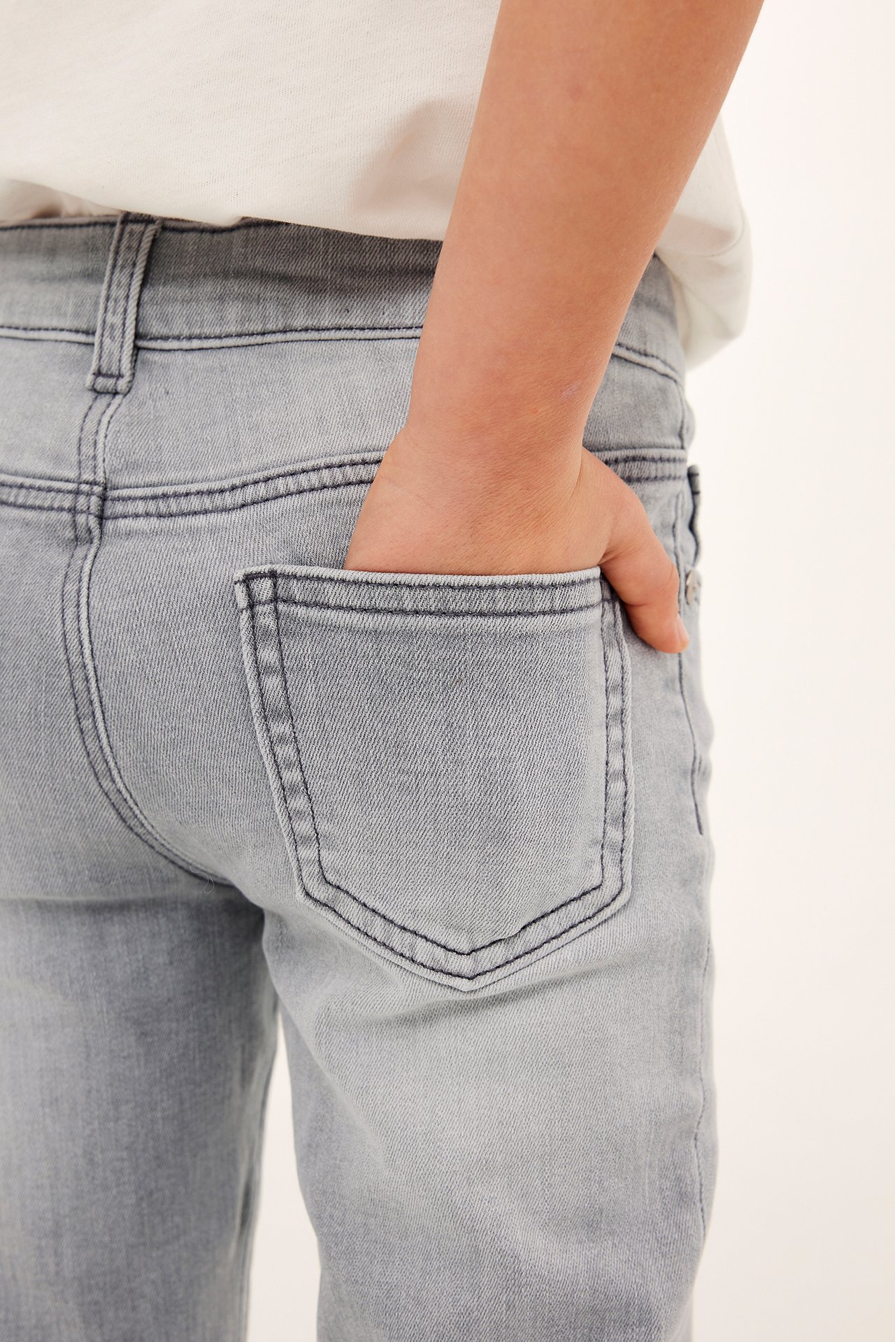 Närbild bakifrån på barn i grå bootcut denimjeans, hand i fickan, vit t-shirt.