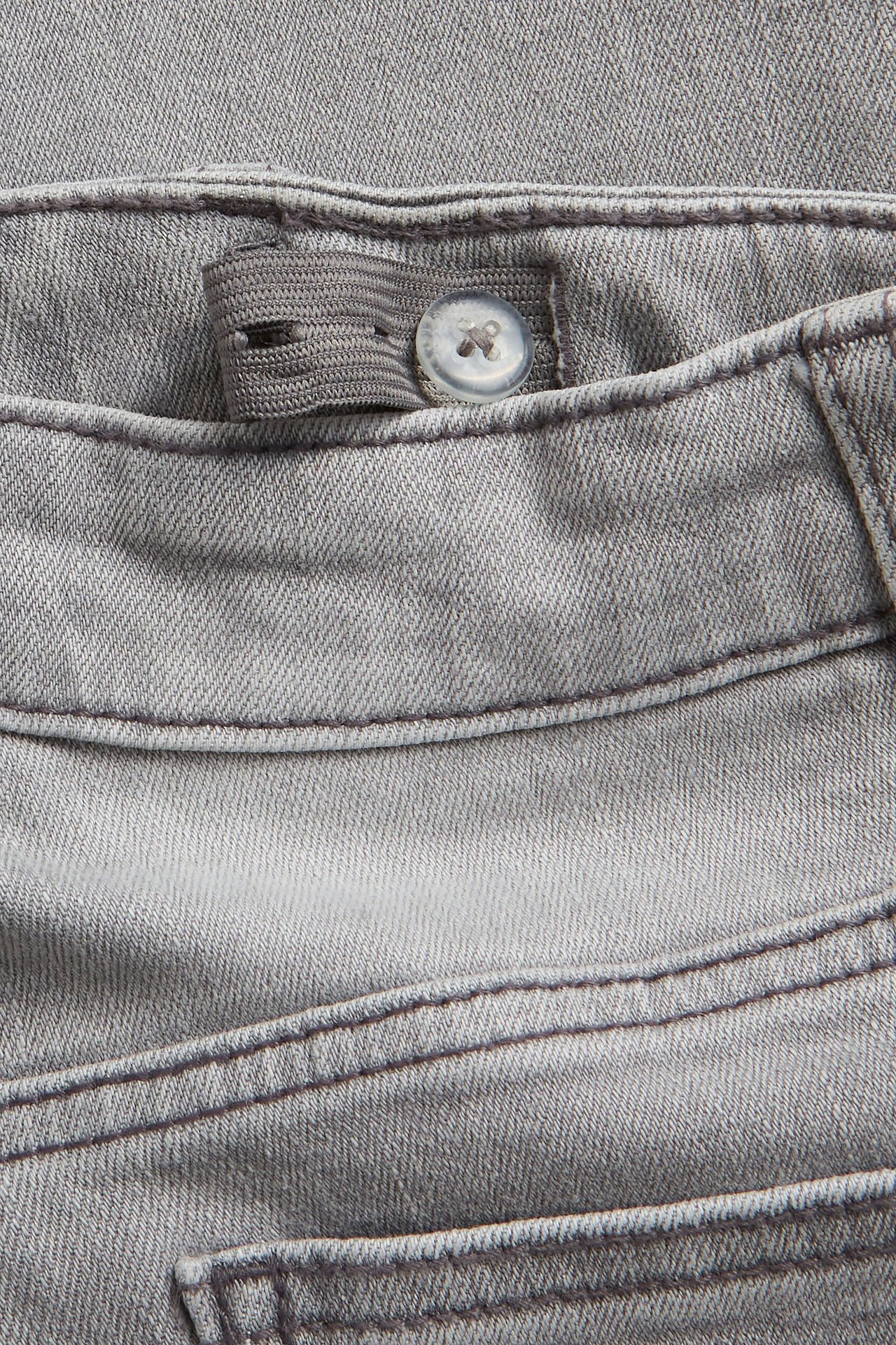 Zbliżenie na pas szarych jeansów bootcut dla dzieci z regulowaną gumką i guzikiem.