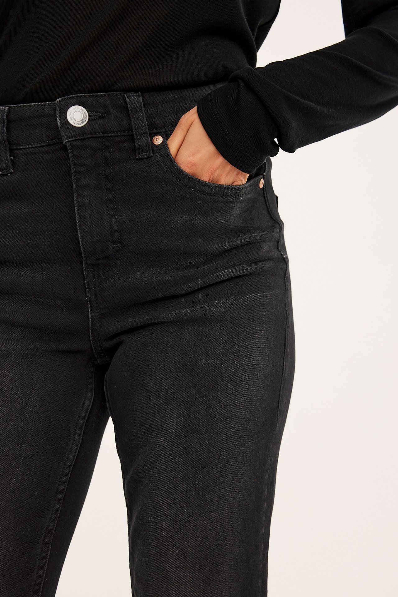 Nærbilde av en kvinne i svarte cropped flare jeans med normal midje og en svart langermet topp.