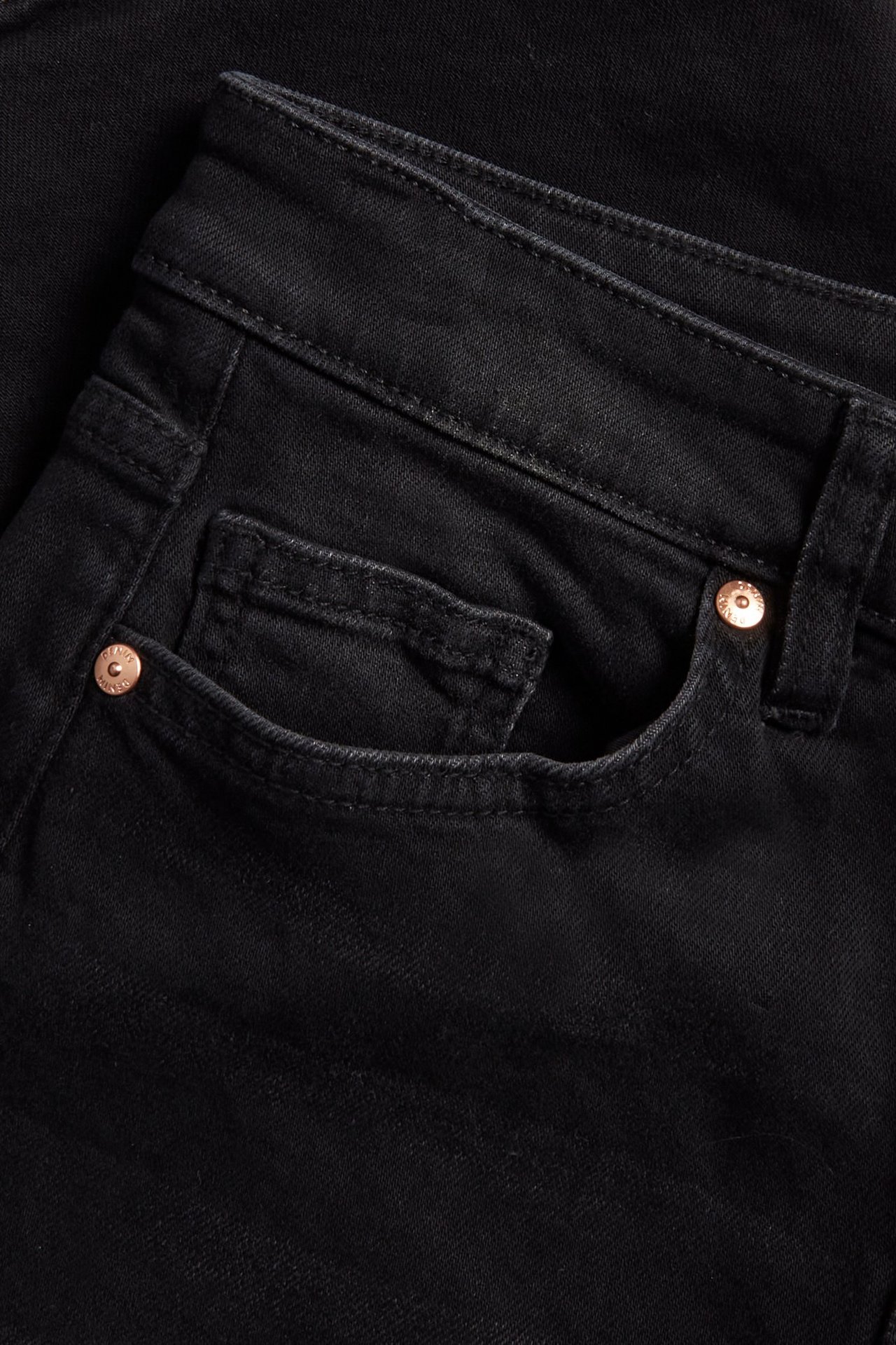Zbliżenie na czarne dżinsy cropped flare z denimu z kieszonką na monety i miedzianymi nitami.