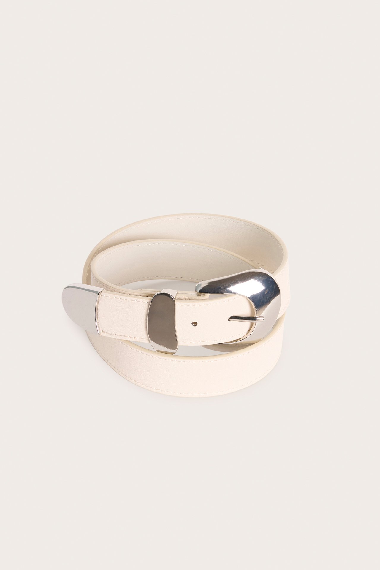 Uppifrån, ett ljusbeige bälte i läderimitation med ett stort silverfärgat metallspänne.