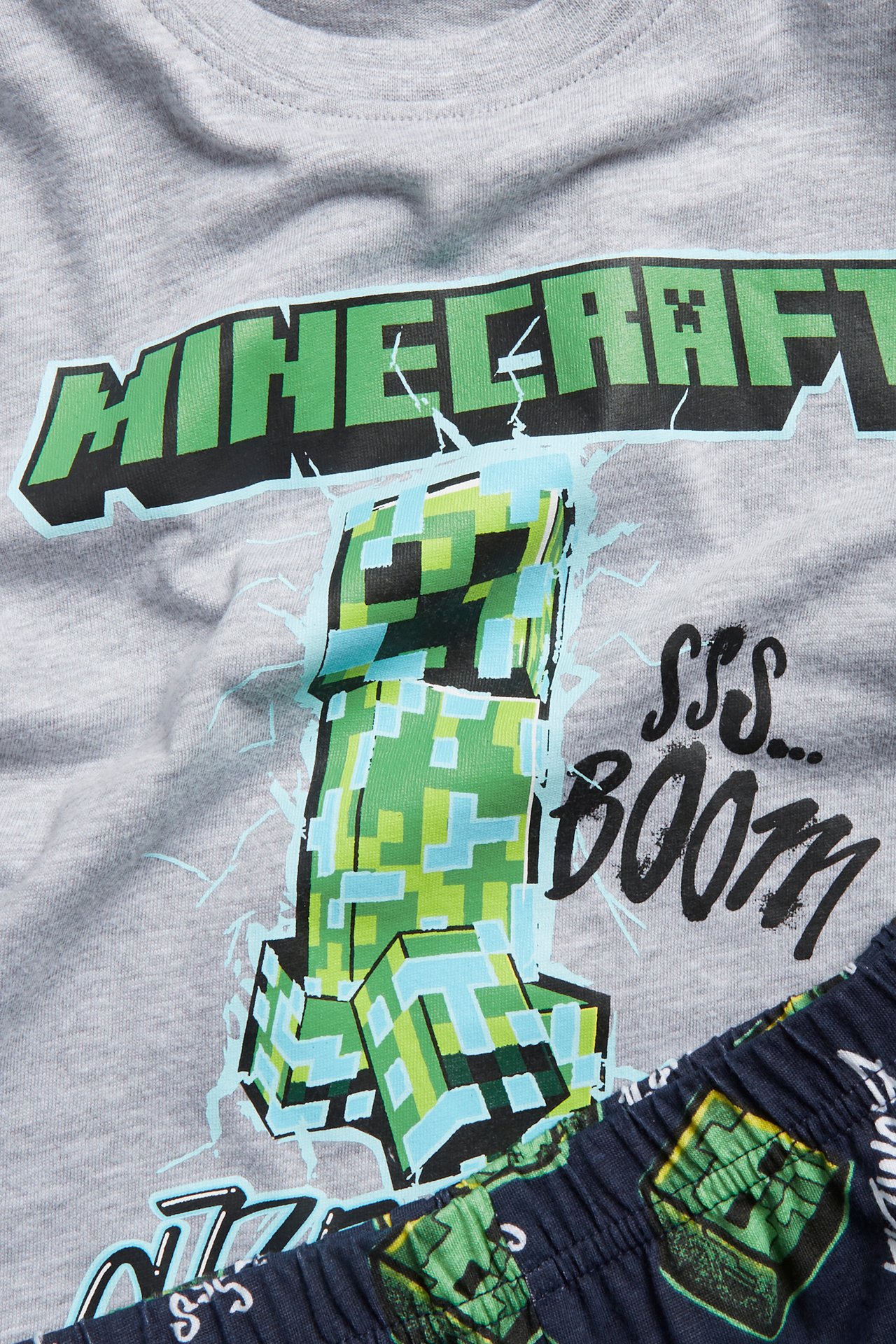 Närbild av en grå kortärmad Minecraft pyjamaströja för barn med Creeper-tryck och mörkblå mönstrade byxor.