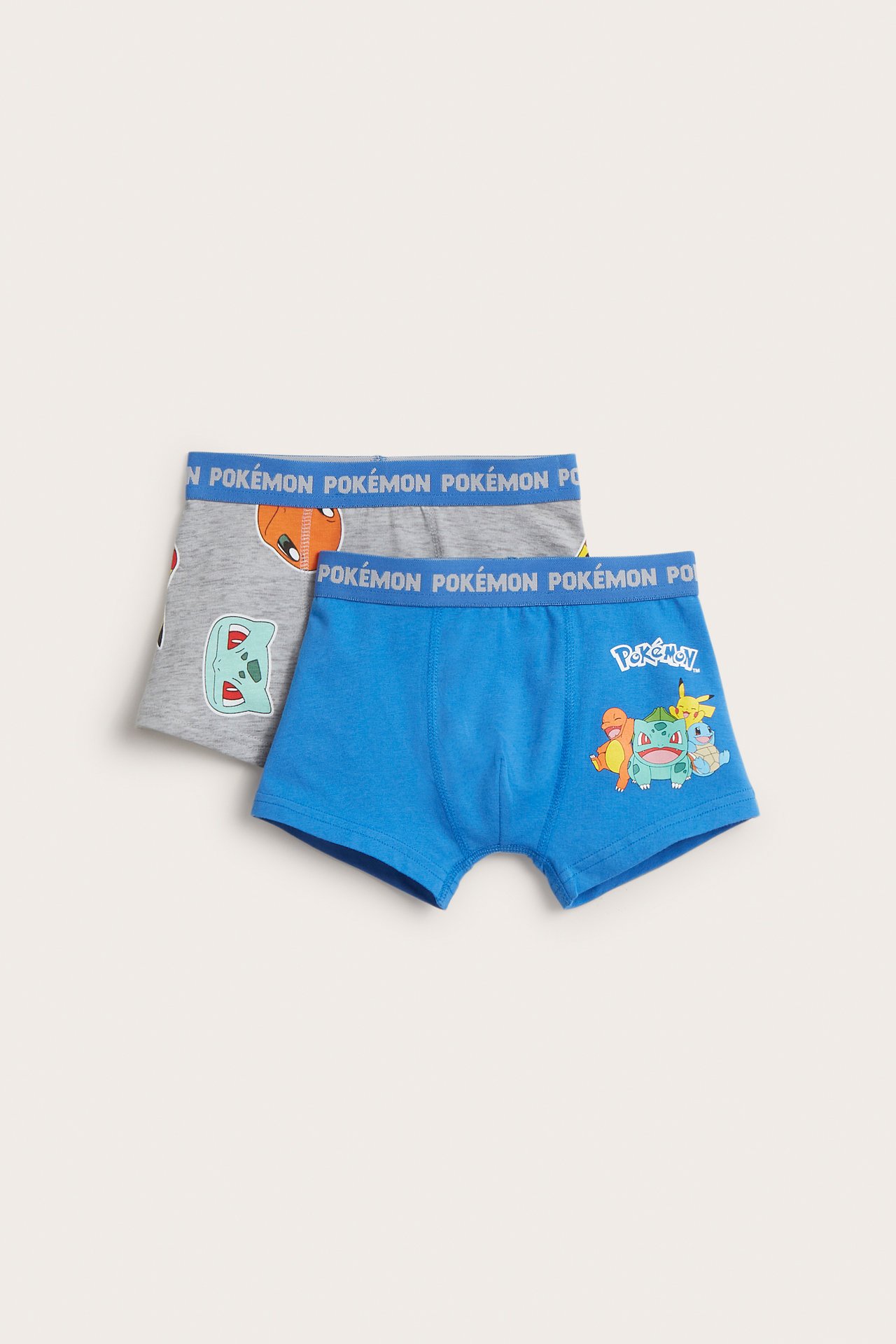 Framifrån: två par barnboxerkalsonger med Pokémon-tryck; en blå med grupptryck, en grå med individuella tryck.