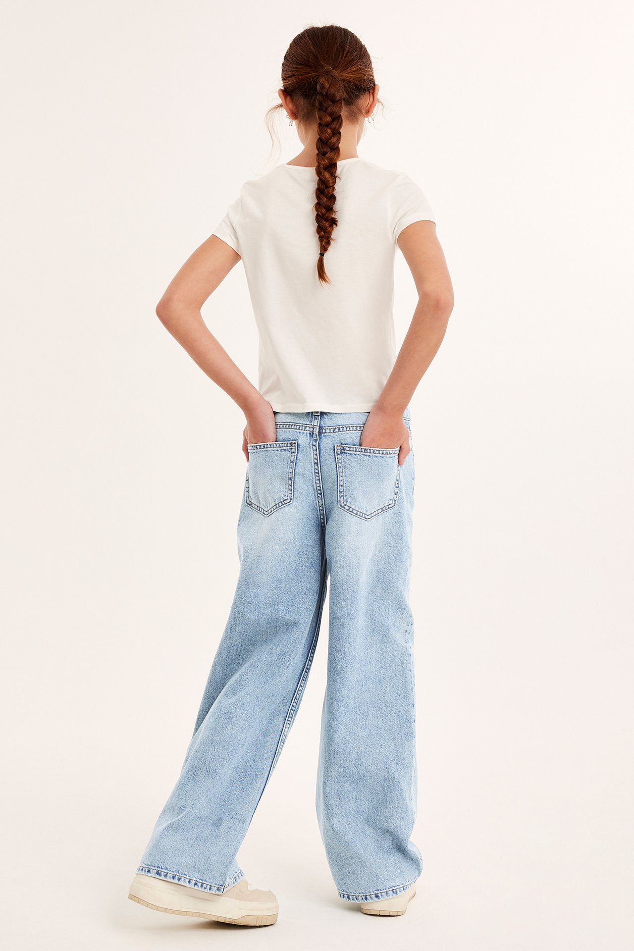 Bakfra: Kid i lyseblå løse jeans, hvit t-skjorte, lyse joggesko. Hendene i lommene.