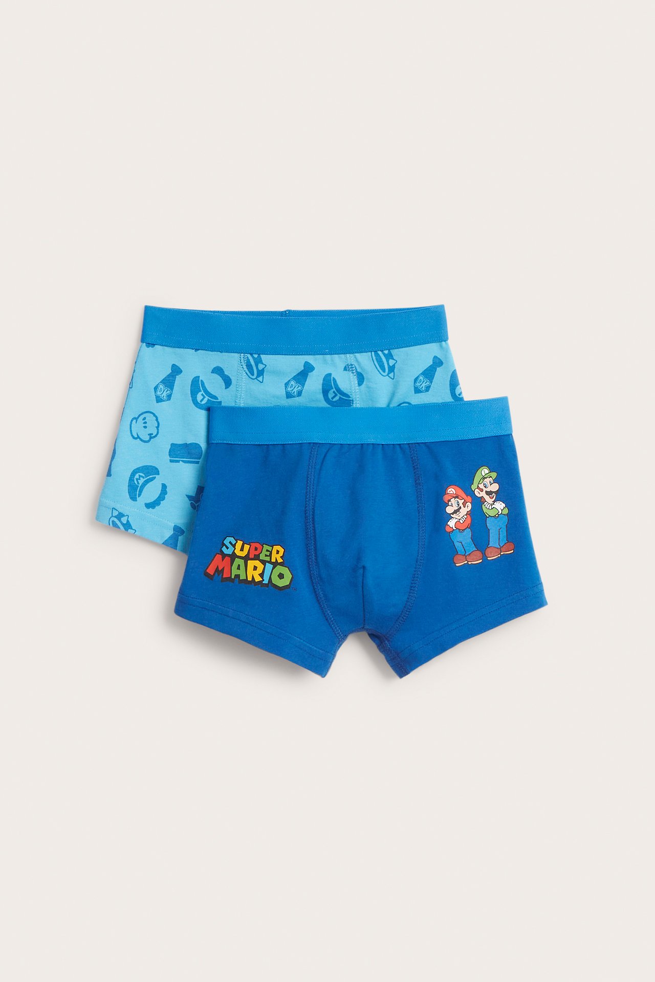 Framifrån, två par blåa barnboxerkalsonger. Det främre paret har Super Mario- och Luigi-tryck, det bakre har ett ikonmönster.