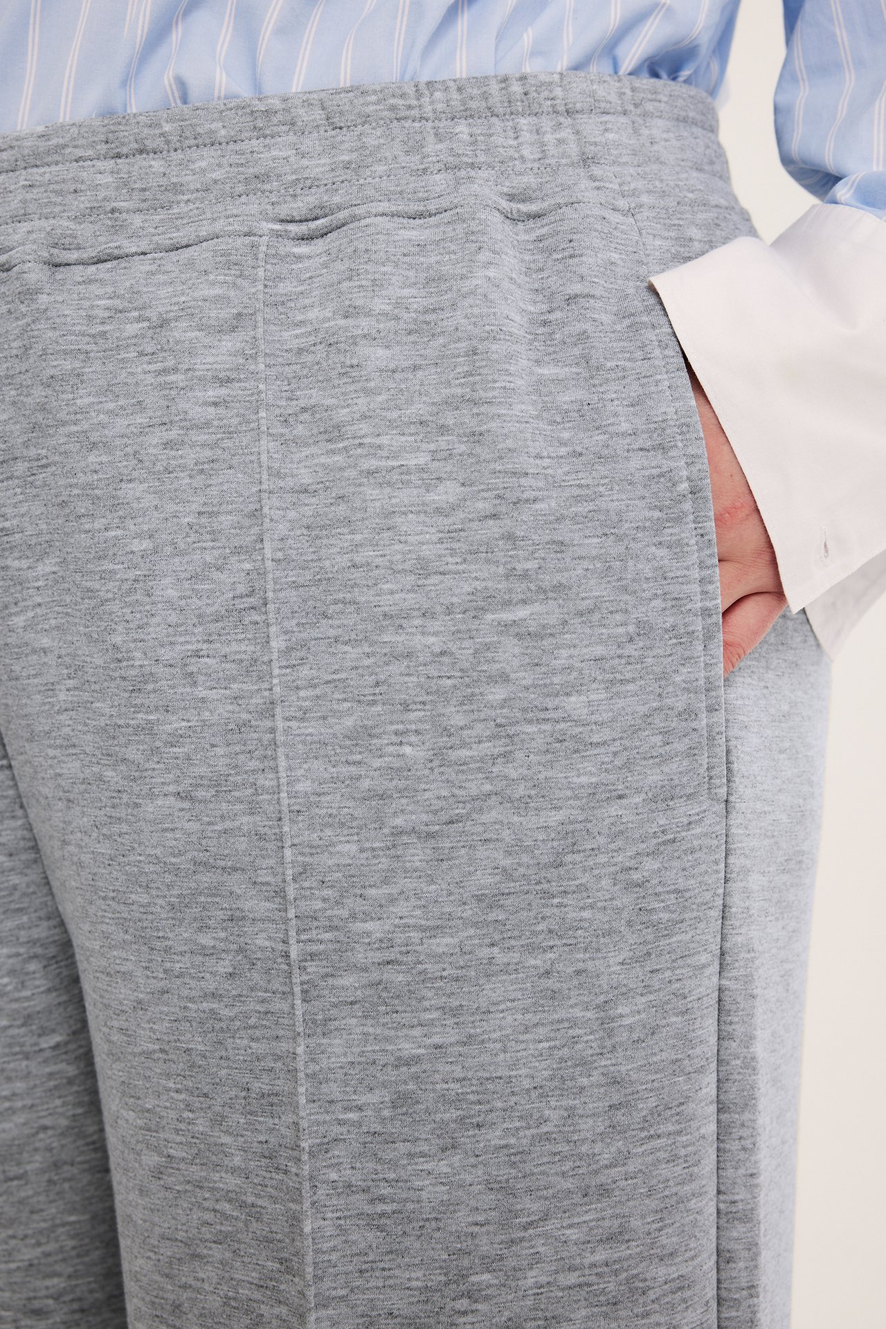 Närbild: damens gråmelerade jersey pull-on byxor med sydda pressveck, hand i fickan och randig skjorta.