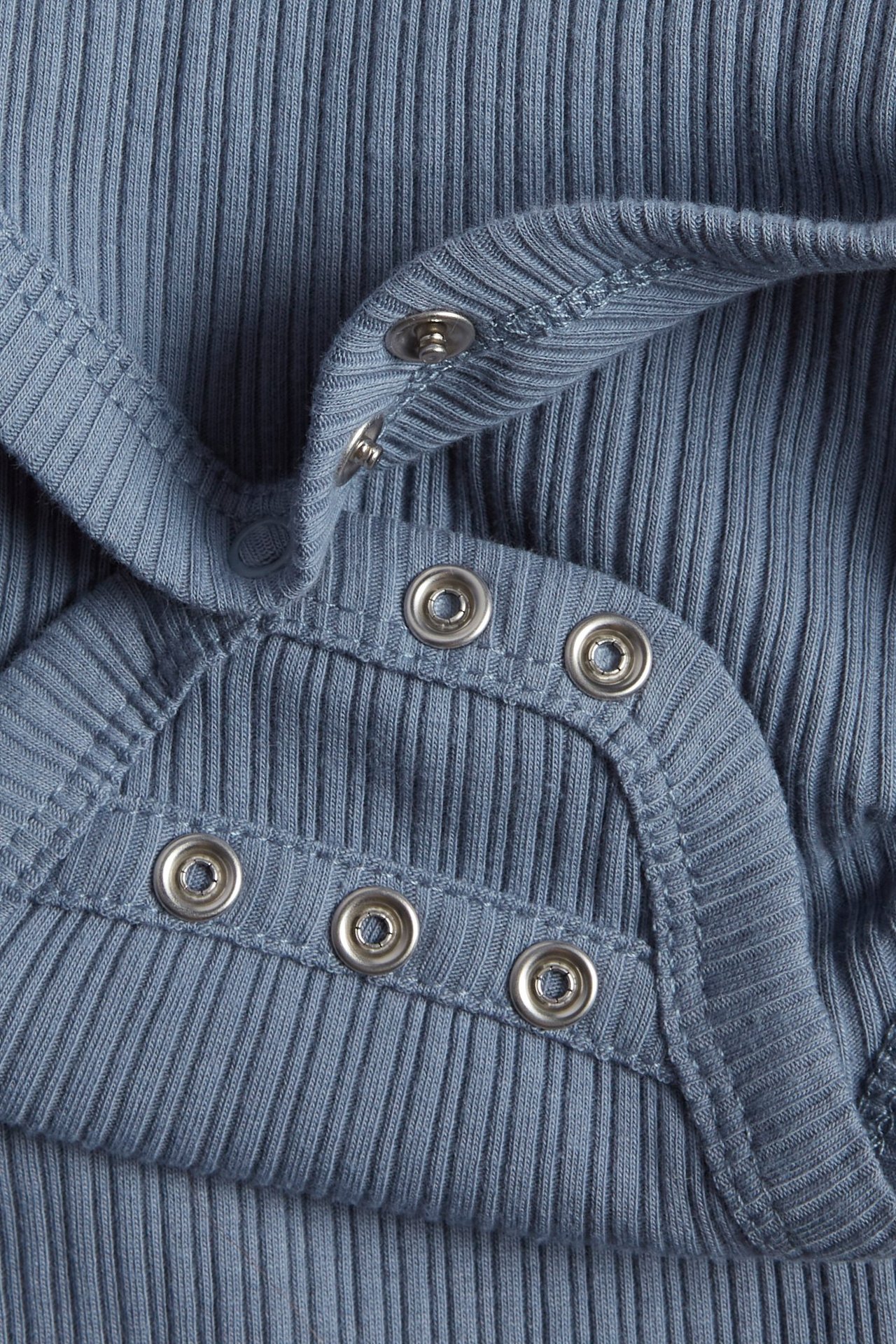 Zbliżenie niebieskiego prążkowanego body kopertowego dla niemowląt ze srebrnymi zatrzaskami.