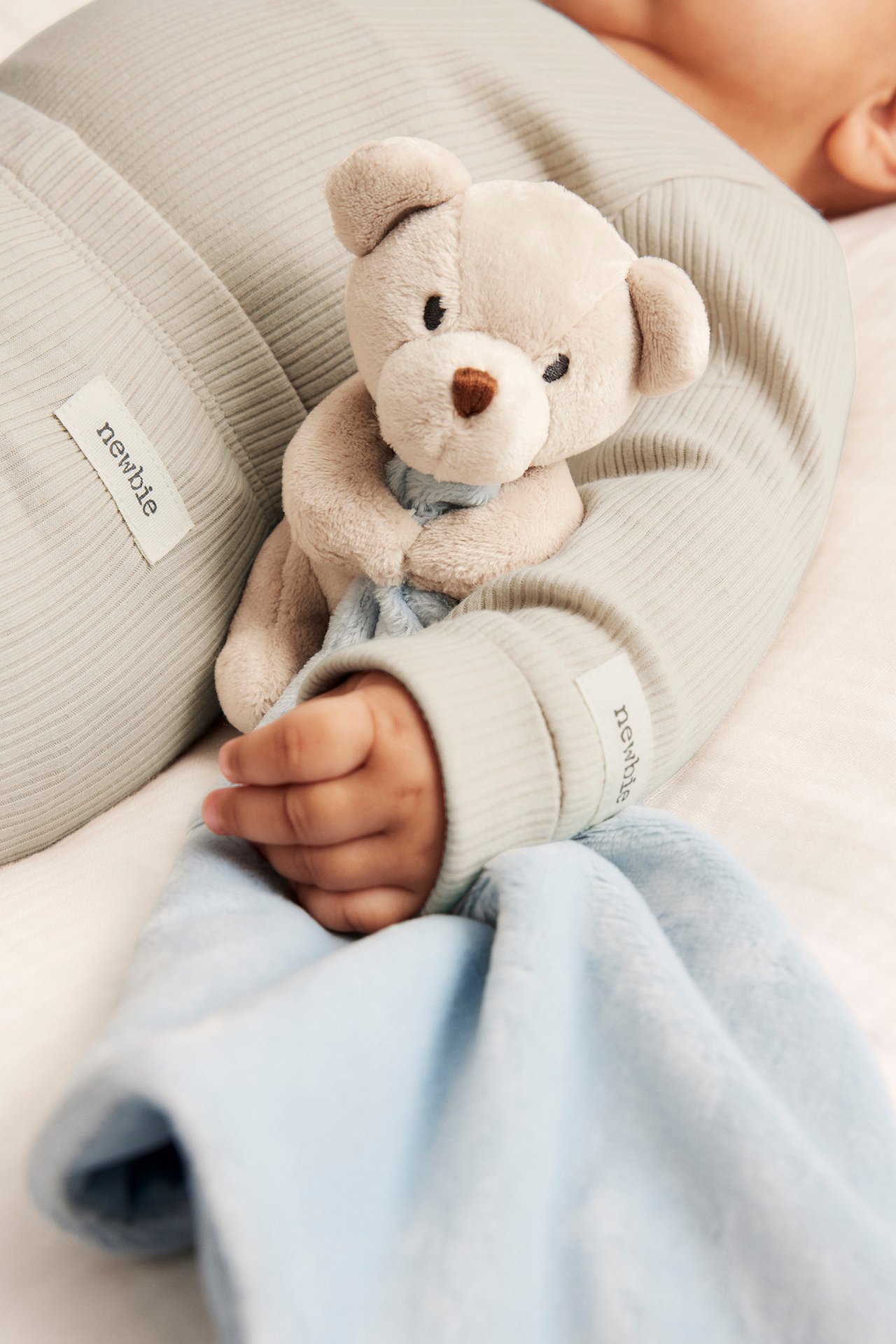 Närbild på baby i ljusgrön ribbad body, håller beige nalle och ljusblå filt.