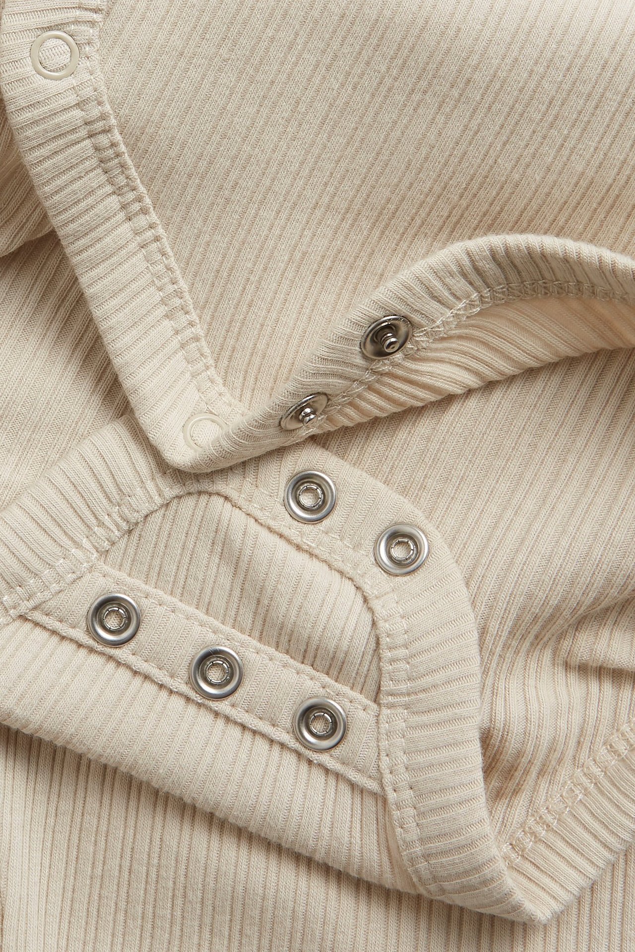 Närbild på en beige ribbad omlottbody för baby med silverfärgade tryckknappar.